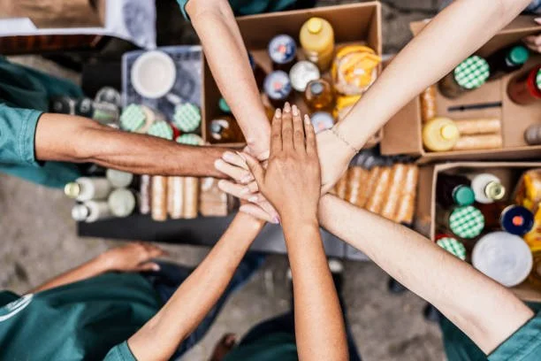 Multiple people stacking hands over a table with bottles and boxes of condiments.