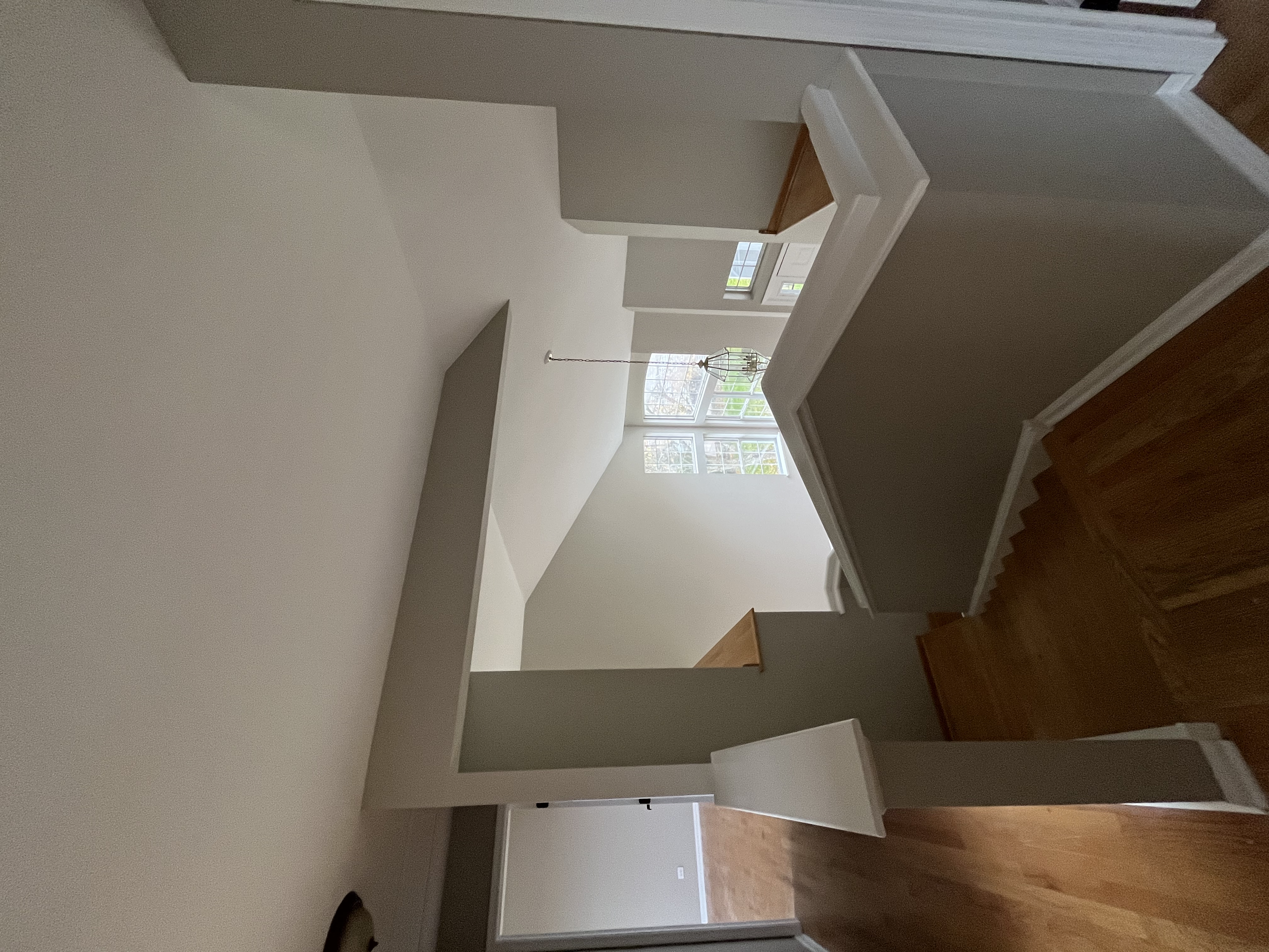 Interior view of a home with a staircase, a white wall, a window with a view outside, and a decorative hanging light fixture.