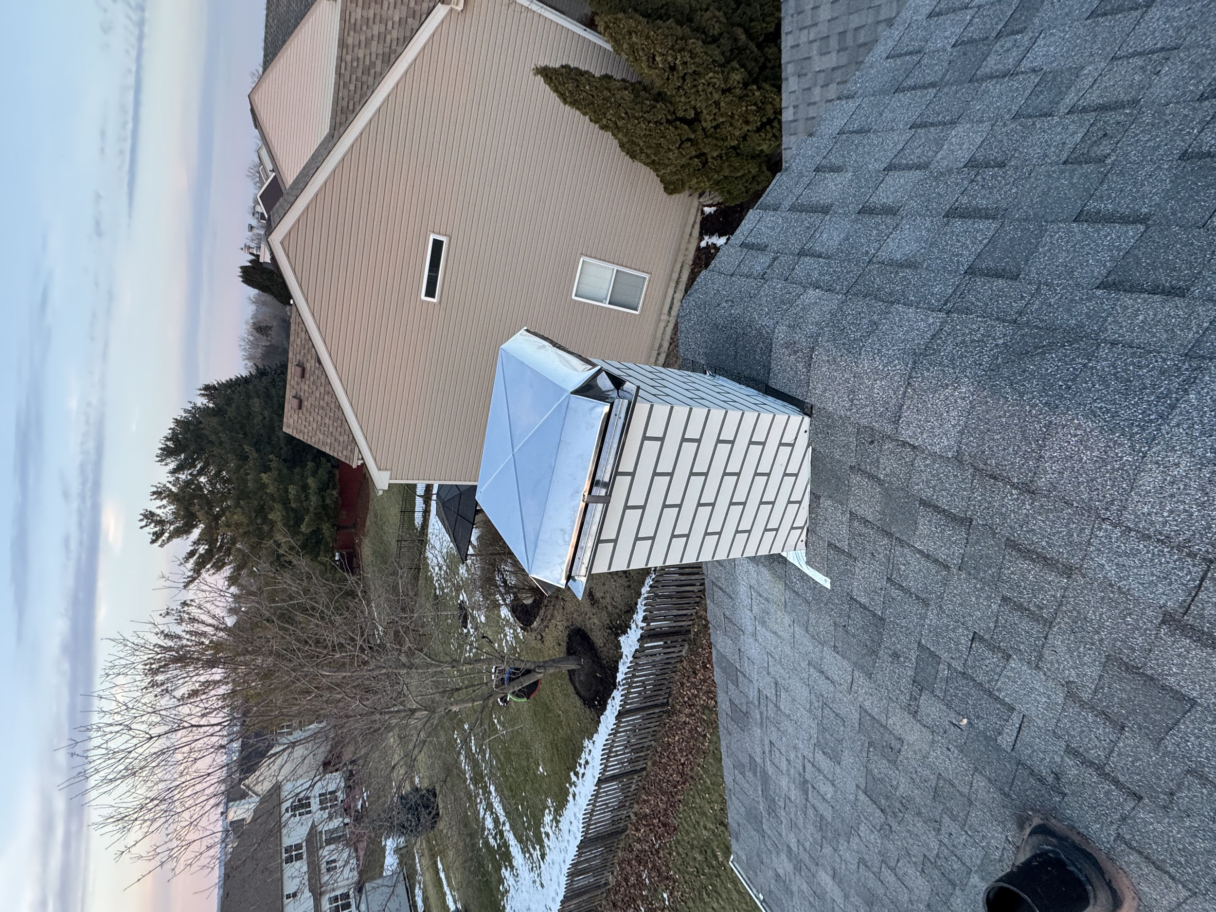 Backyard with a deck, a small well-maintained garden, trees, and a house in the background, taken during winter with patches of snow on the ground.