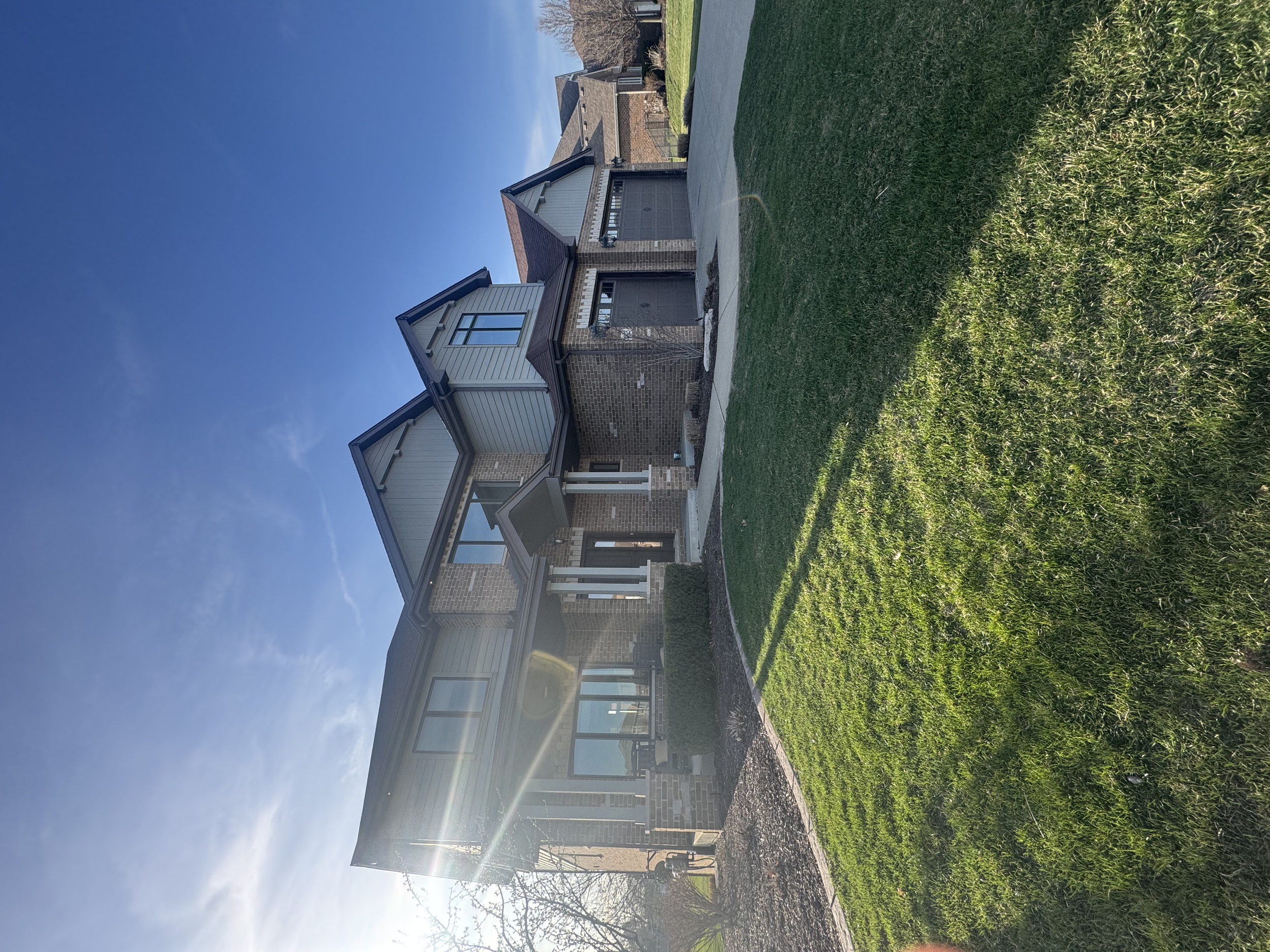 Front view of a modern brick house with large windows, a garage, and a driveway, surrounded by a well-maintained green lawn and a clear blue sky.