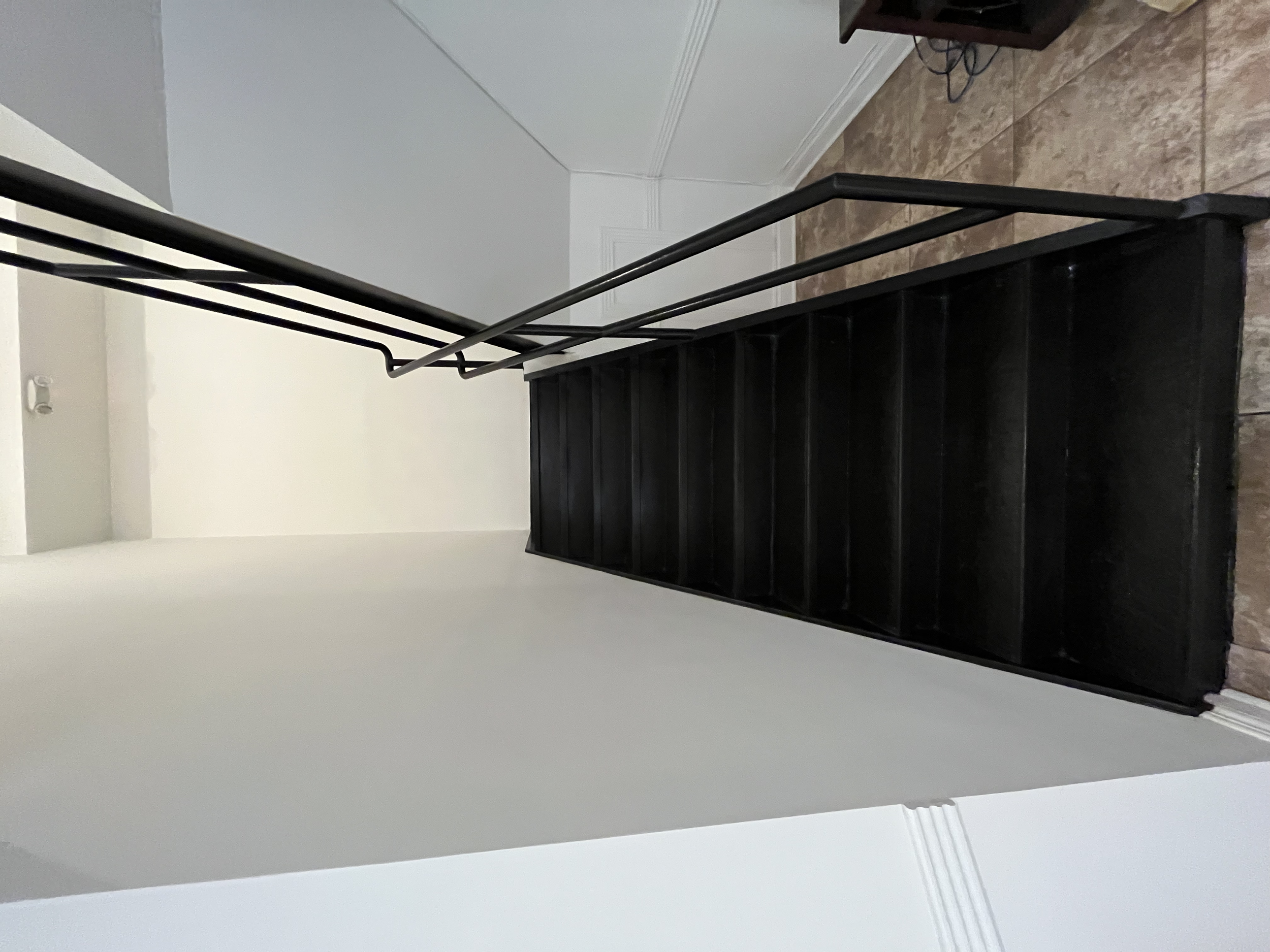 A staircase with black steps and a black metal handrail in a room with tile flooring and white walls.