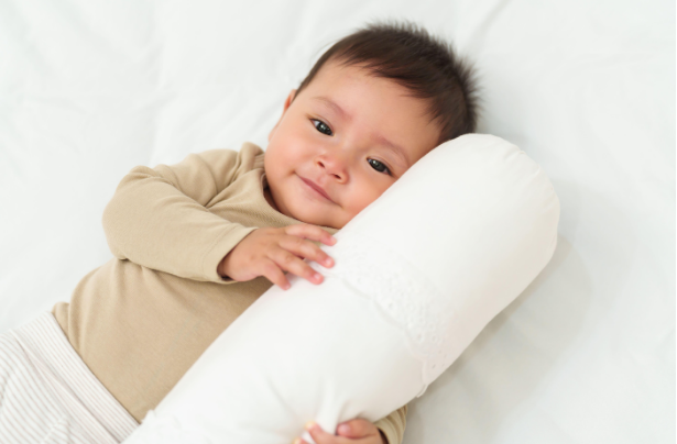 A young child lying on a bed, holding a white pillow, and smiling gently.