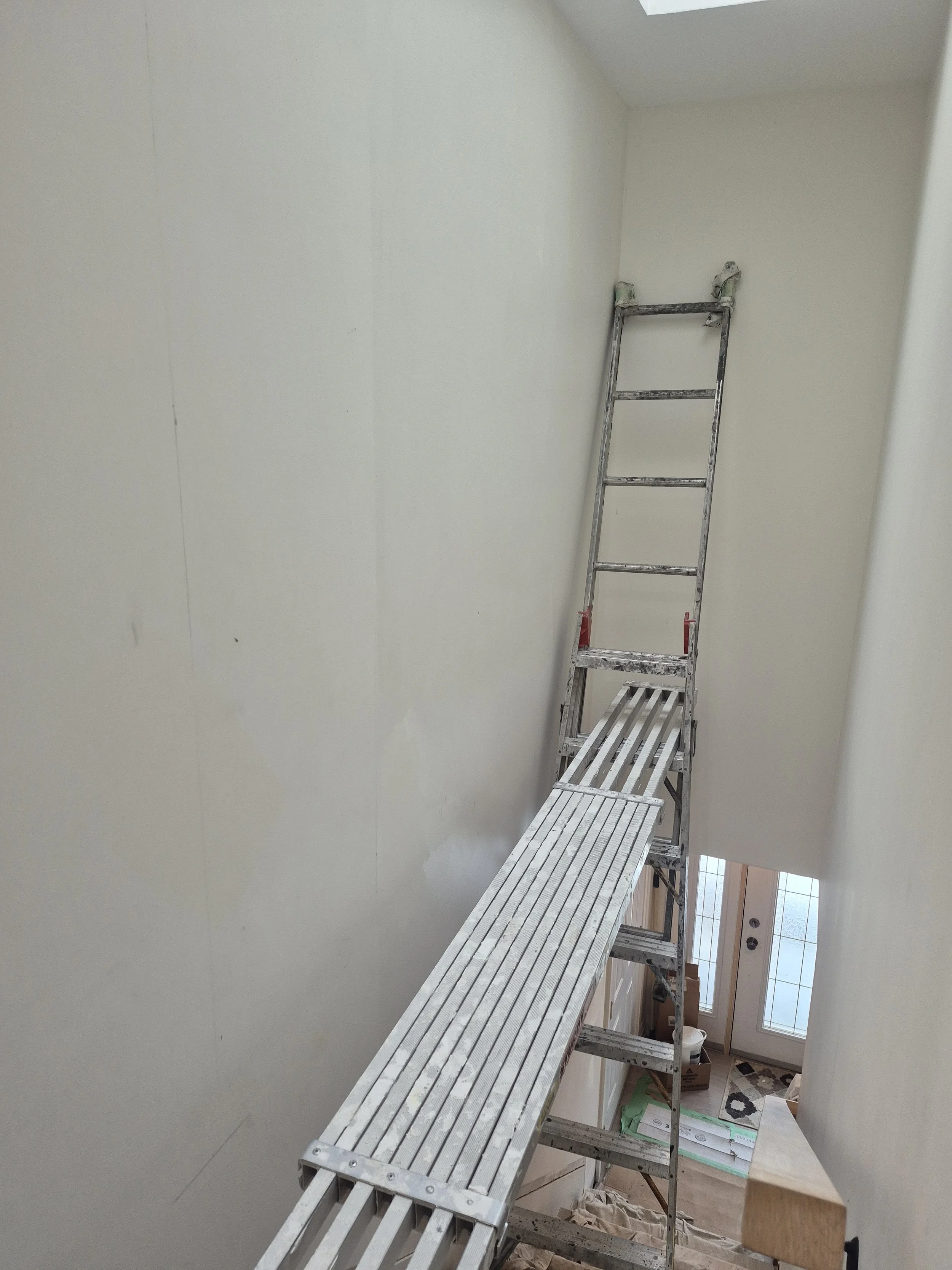 Interior view of a staircase with a ladder and a temporary platform for painting or renovation, with a door at the bottom.