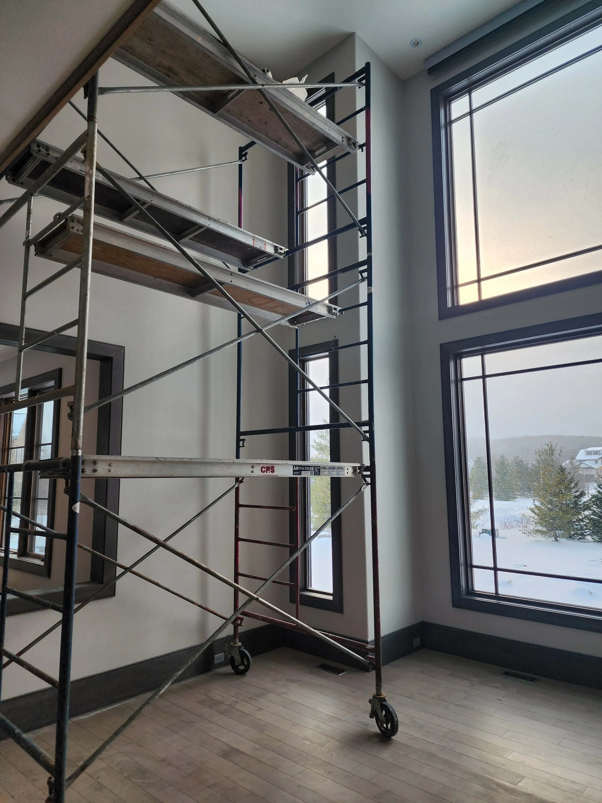 Interior of a room under renovation with a metal scaffold near large windows showing a snowy landscape outside.