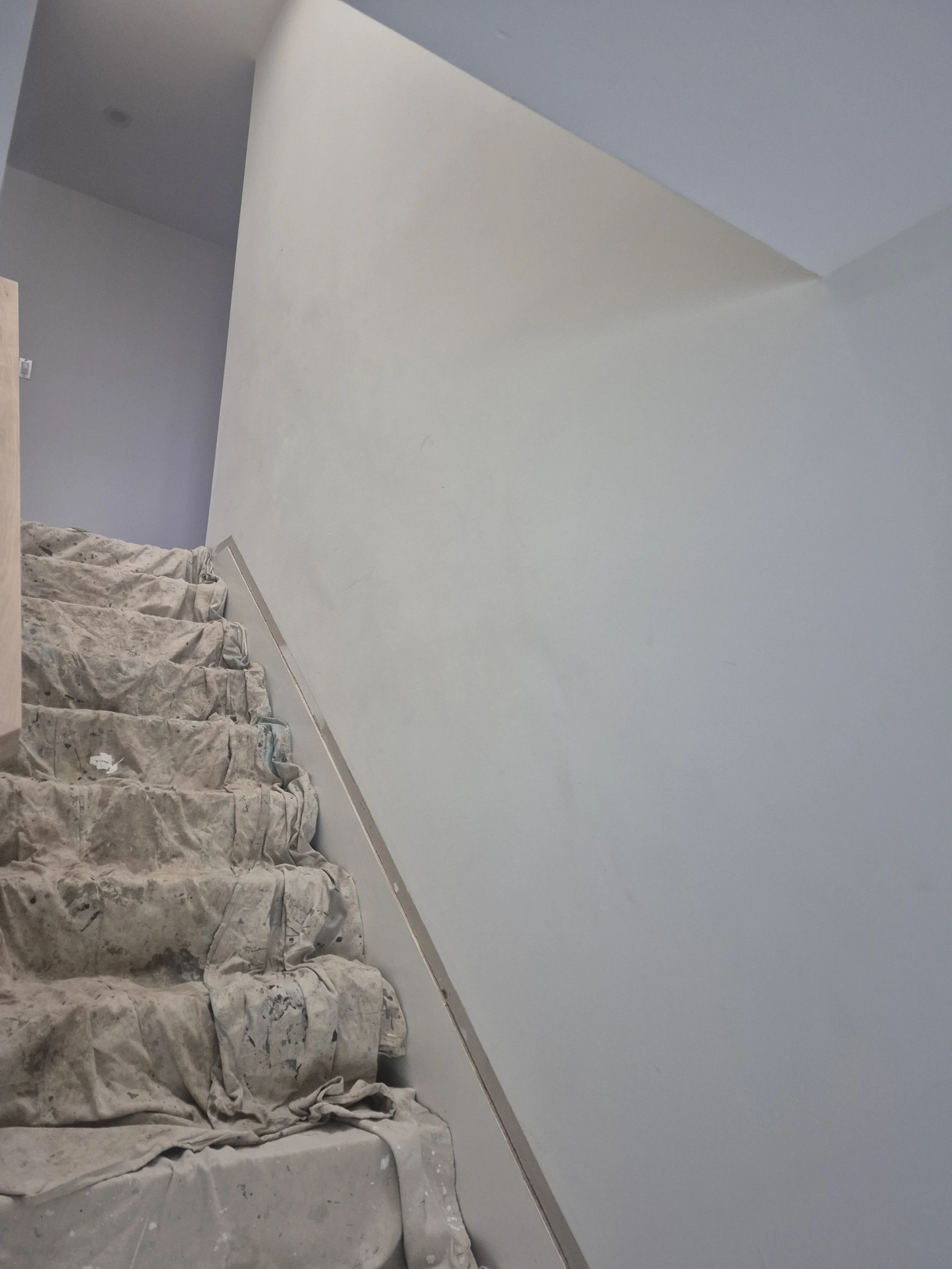 A staircase covered in drop cloths with paint splatters, leading up to a wall being painted or dried.