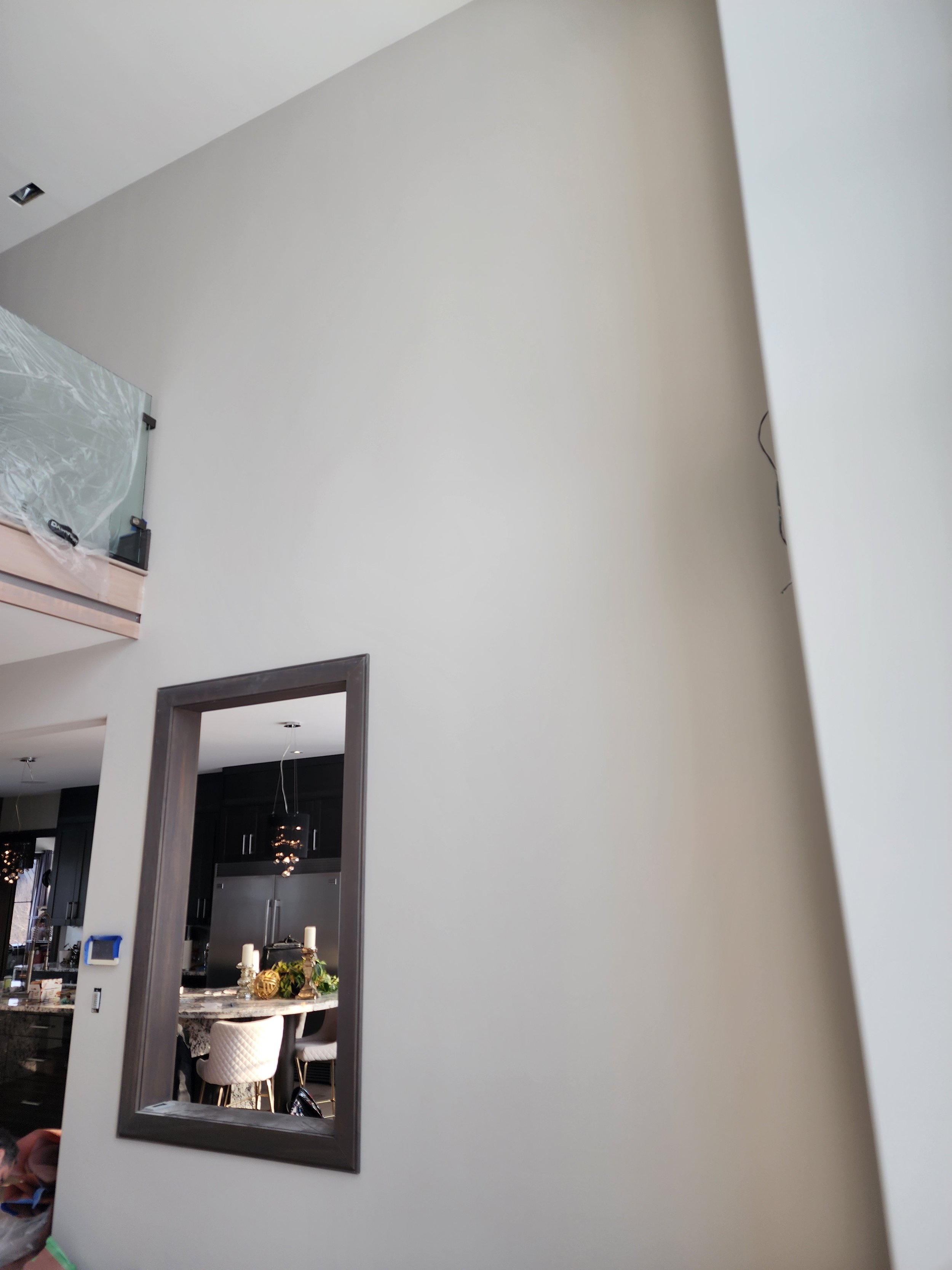 Interior of a modern home with a neutral-colored wall, a large mirror, and a kitchen visible through a doorway, decorated with holiday ornaments and candles.