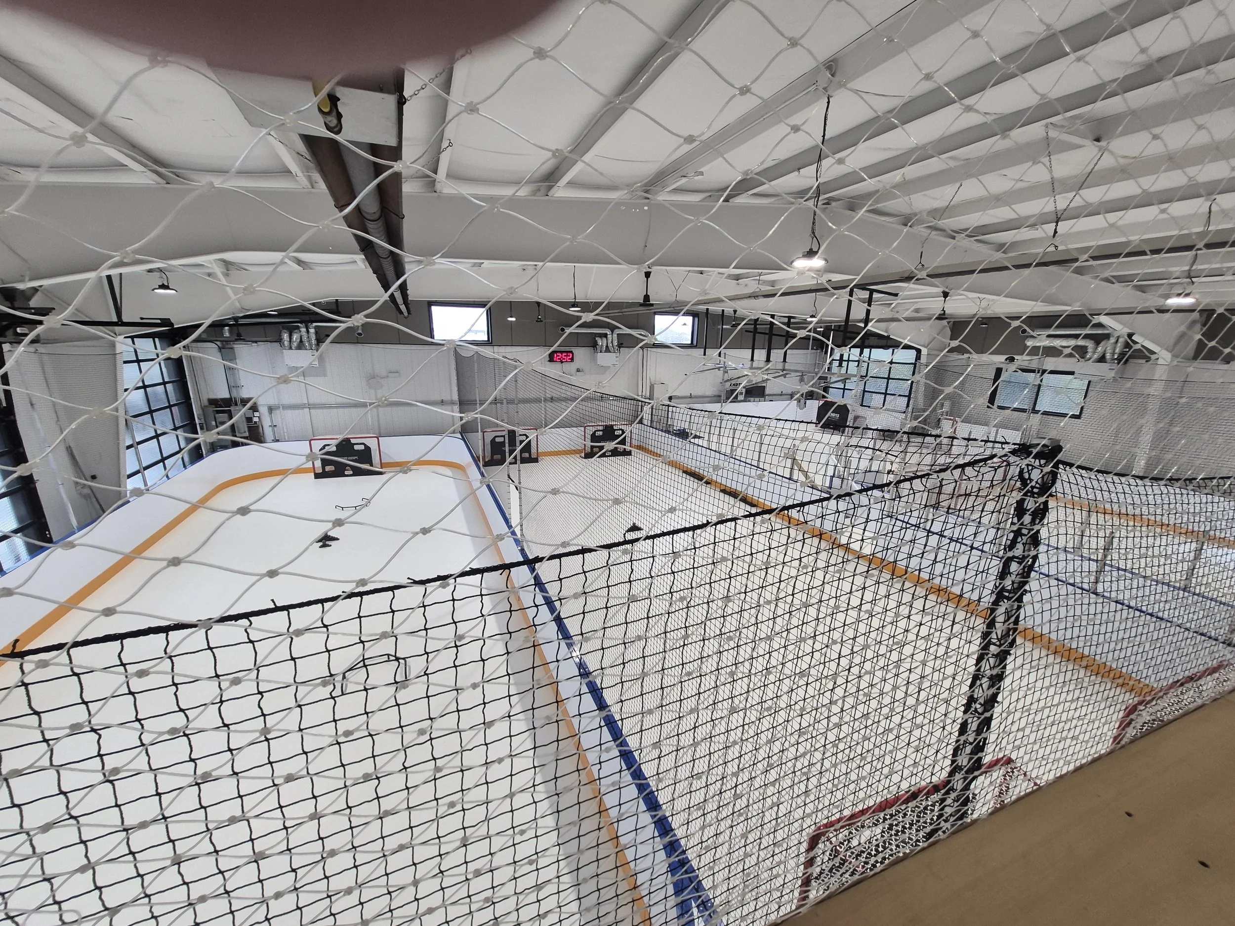 Indoor hockey rink with nets and goals, viewed through a safety net.