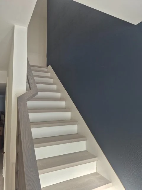 Interior staircase with white steps, a light wood handrail, and a dark blue wall on one side.