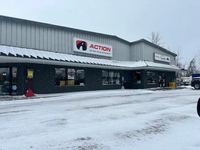 Exterior of a store called Action Car and Truck Accessories with snow on the ground and roof, parked cars nearby.