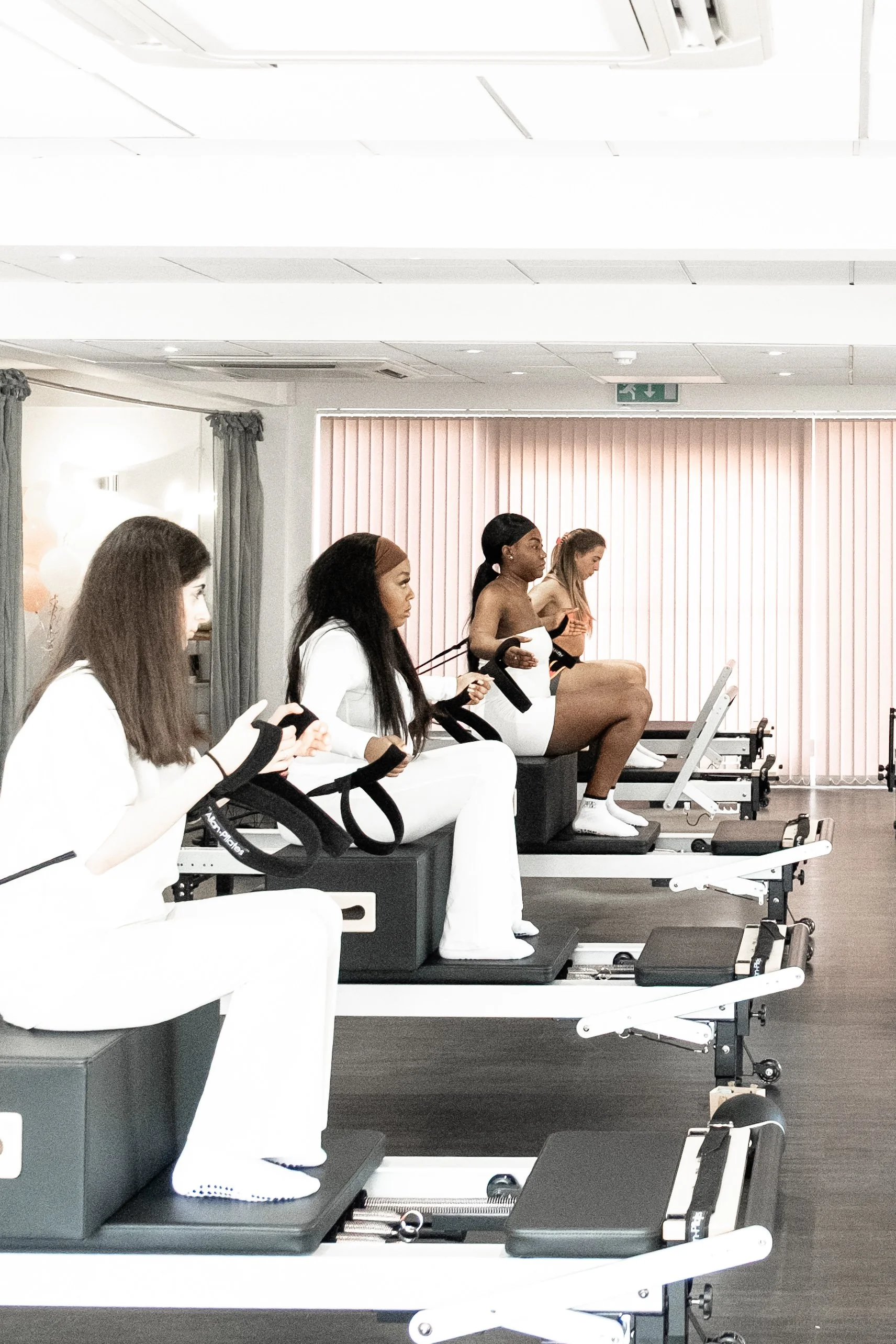 Group of women exercising on reformer Pilates machines in a fitness studio.