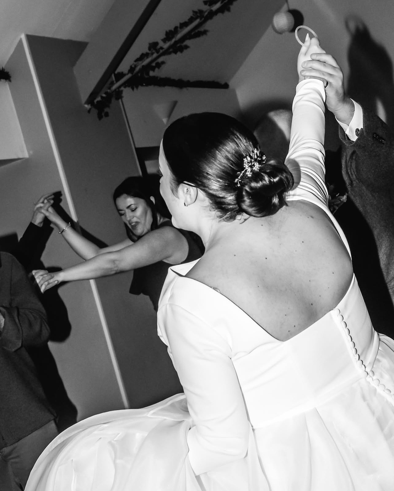 A bride in a wedding dress dancing with a partner at her wedding reception, with another woman dancing in the background.