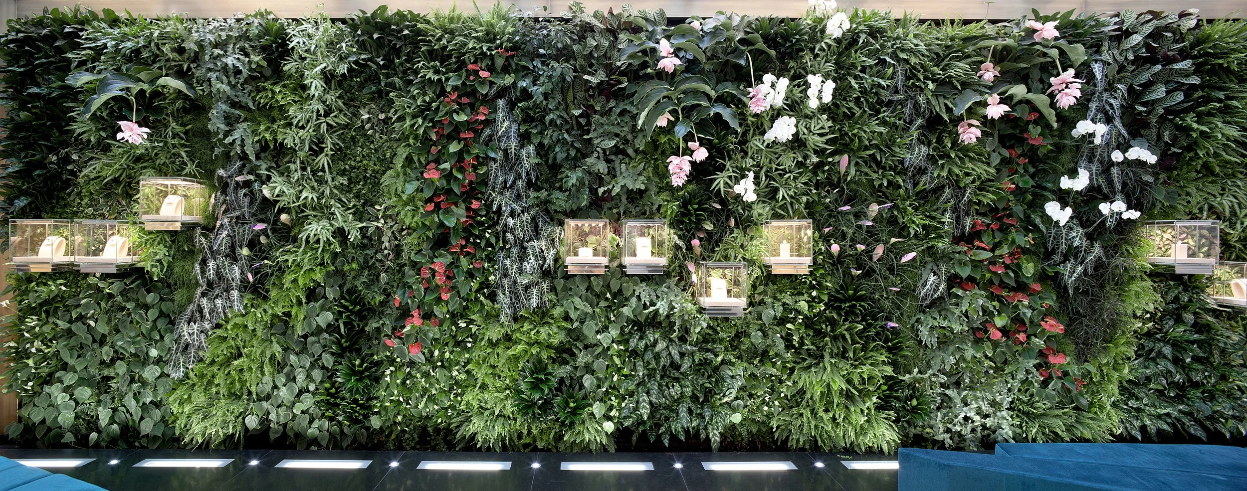 Parete verde decorativa con piante e fiori, con alcune luci e scatole contenenti candele