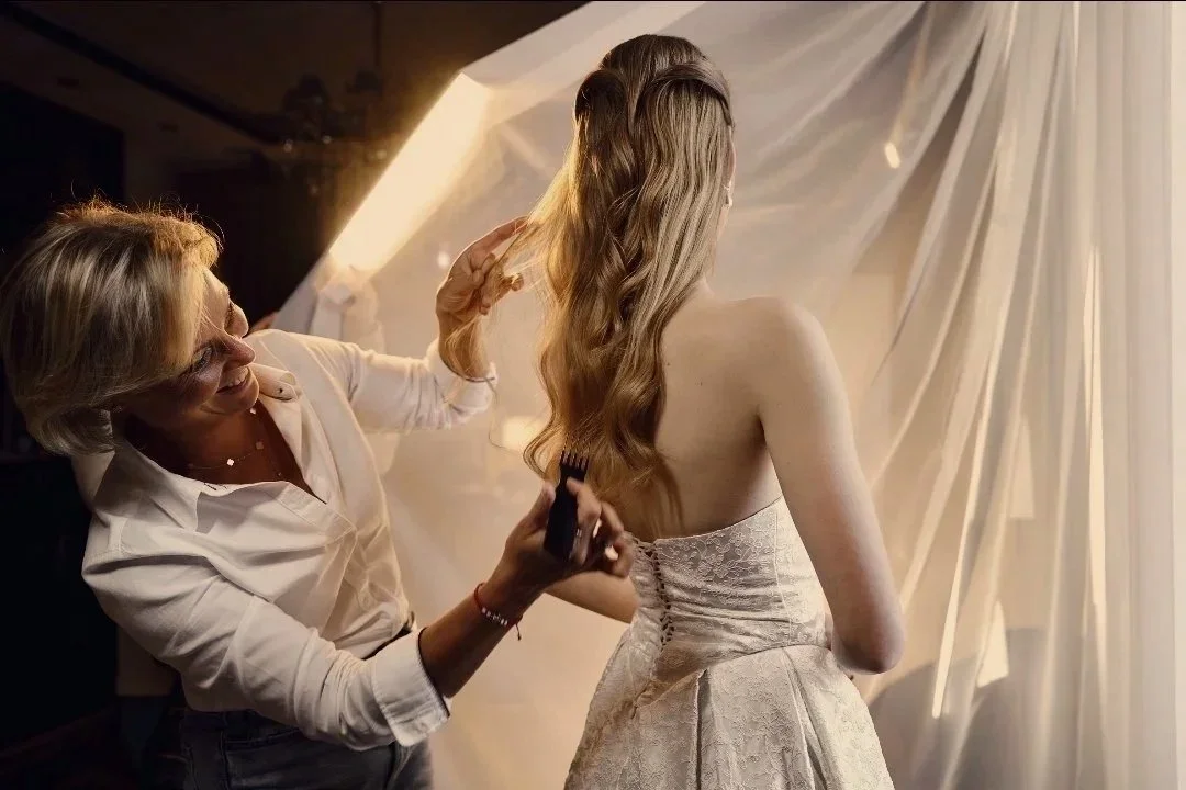 Friseurmeisterin stylt einer jungen Frau mit langem, gewelltem Haar bei einem Fotoshoot in einem luxuriösen Raum.