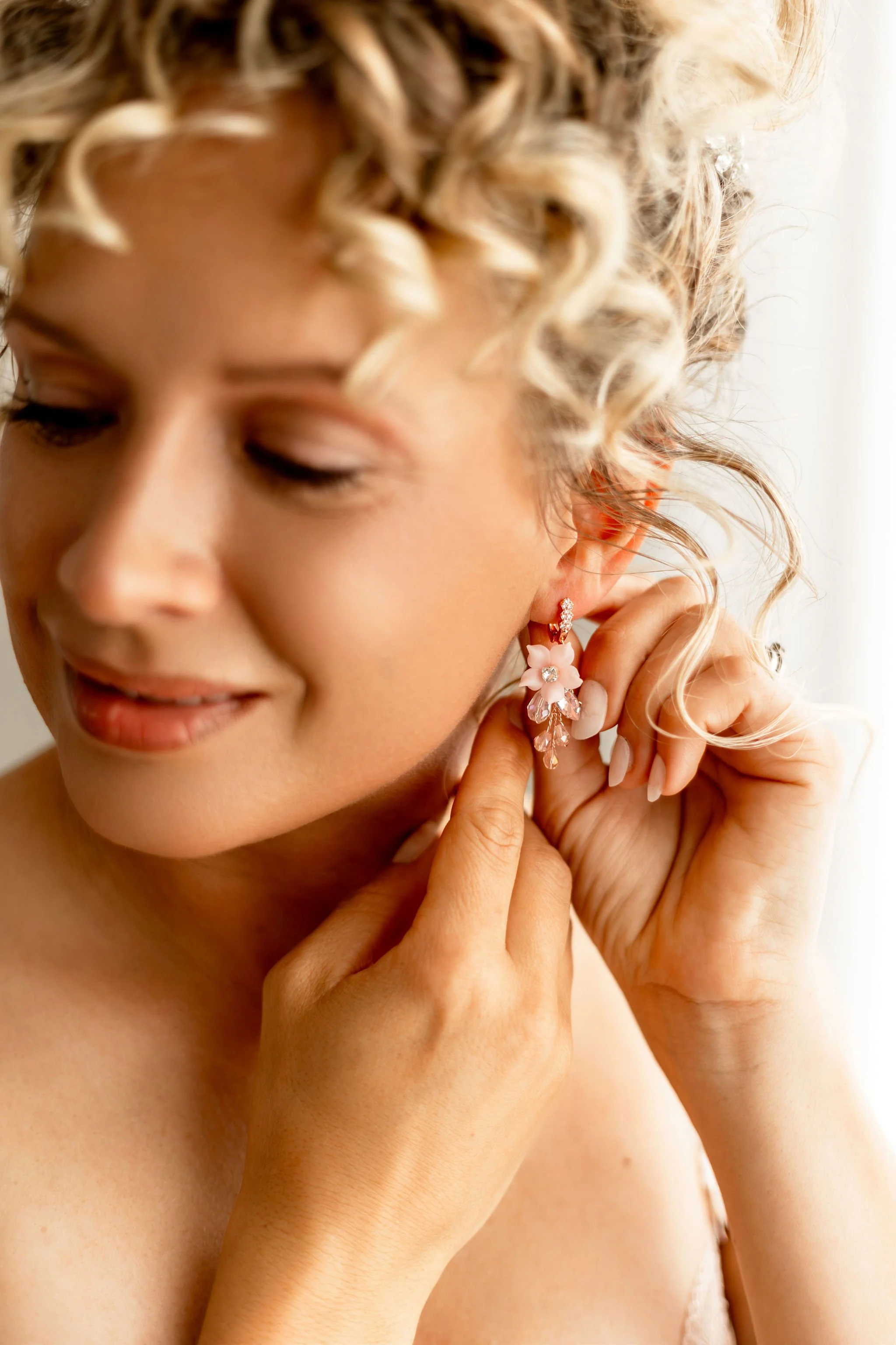 Nahaufnahme einer Frau mit lockigem blonden Haar, die ein elegantes großes Ohrring mit Blumen- und Kristallelementen trägt.