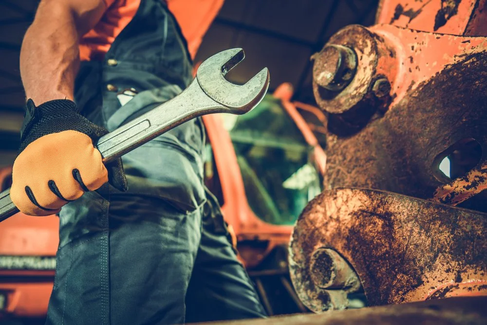 Person holding a wrench next to a rusty, large metal machinery or part.