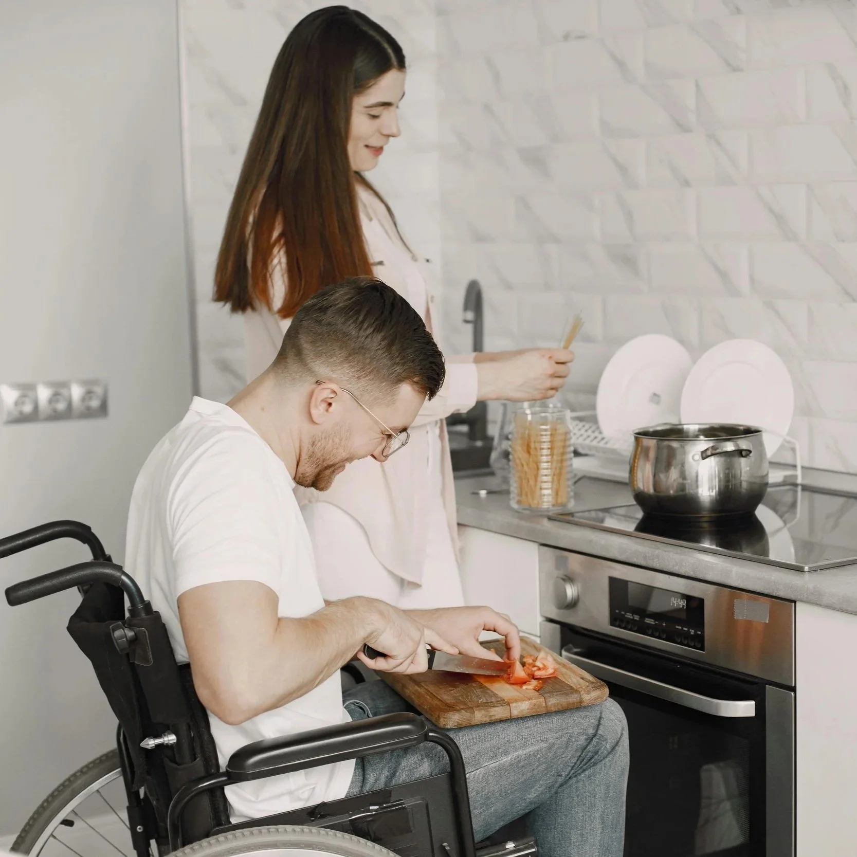 A young able bodied lady and a young man in a wheelchair prepare dinner.  Occupational therapy cooking skills