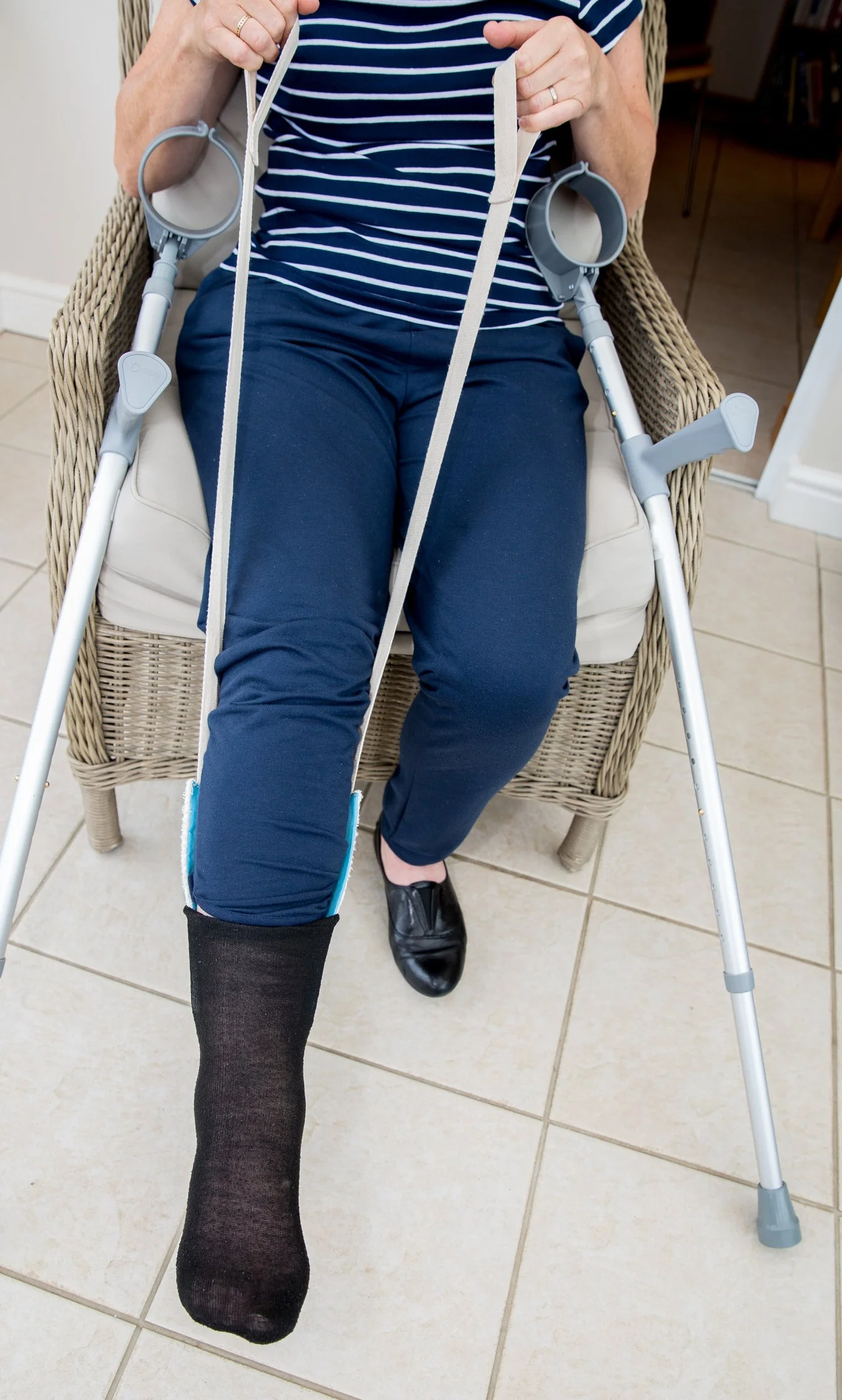 lady using a sock aid and crutches following injury.  Having rehabilitation.