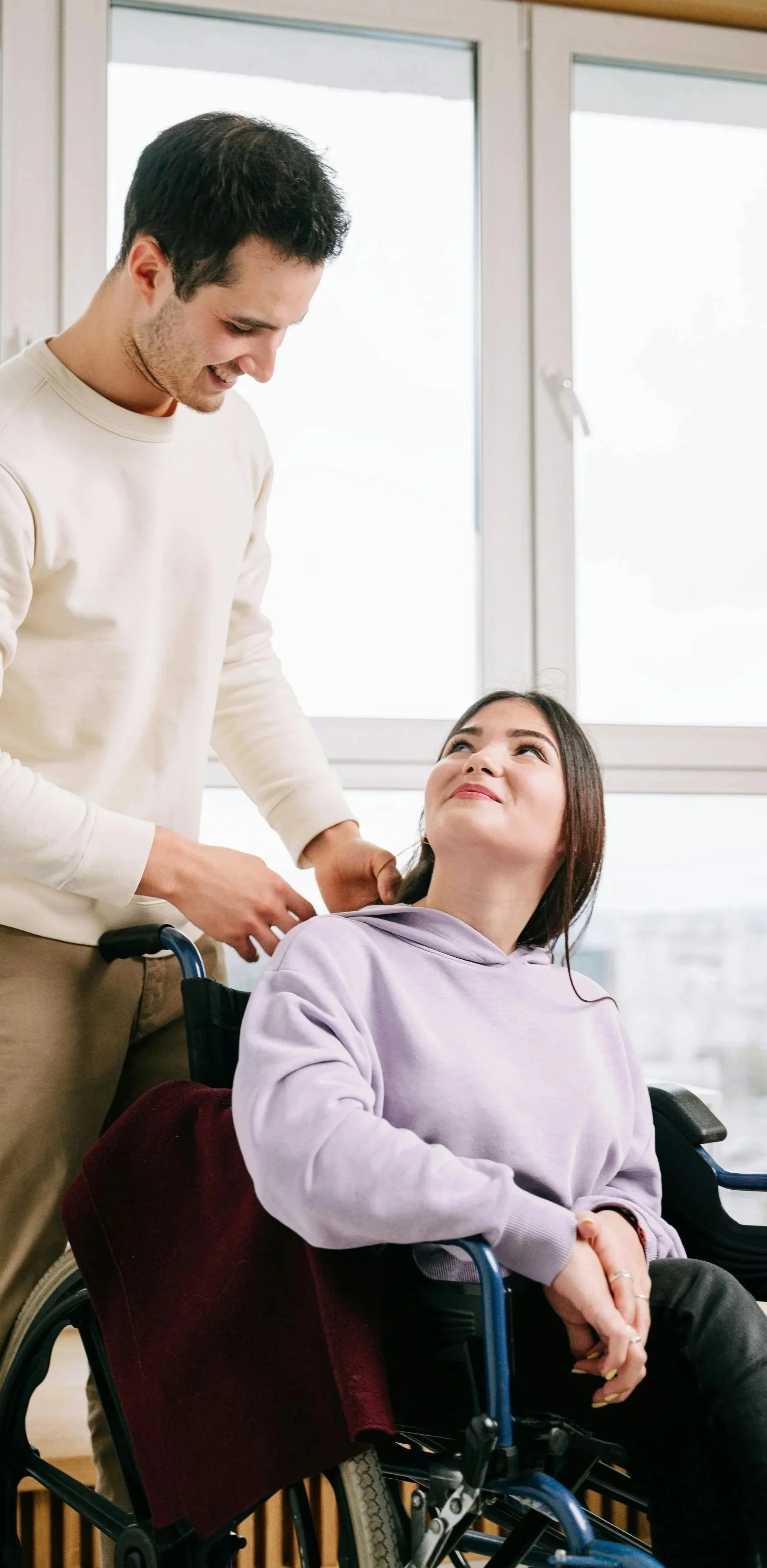 A young lady in a wheelchair looking round and a young man.  Occupational Therapy