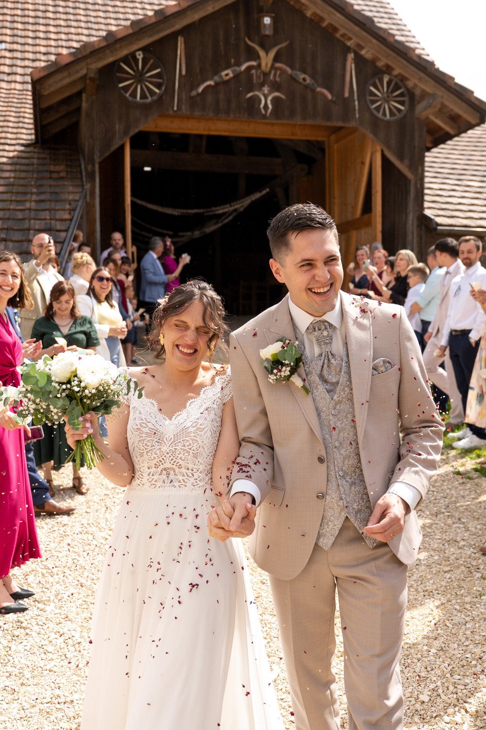 Couple de mariés lors de leur sortie de mariage en suisse, haie d'honneur de leurs invités. Par Viviane Eyer, Photographe de mariage basée dans le Grand Est
