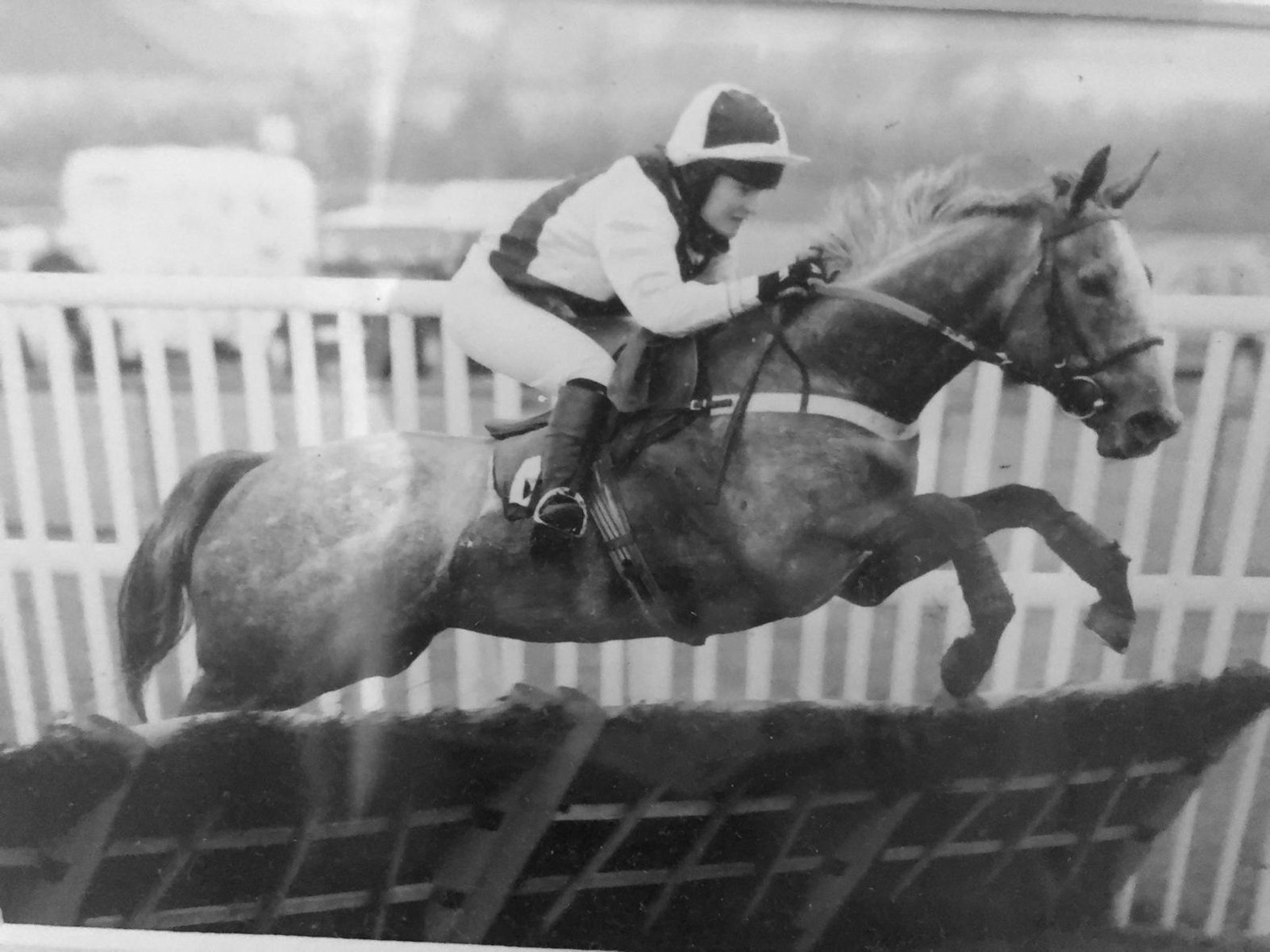 Black and white photo of a jockey riding a horse over a hurdle in a horse race.