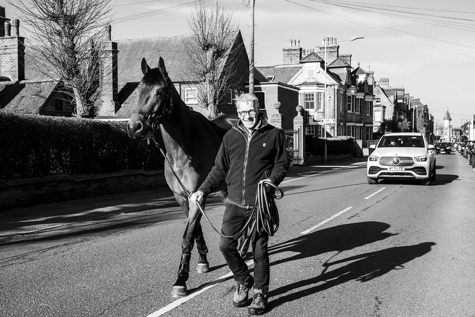 A man walking a horse on a city street in black and white.