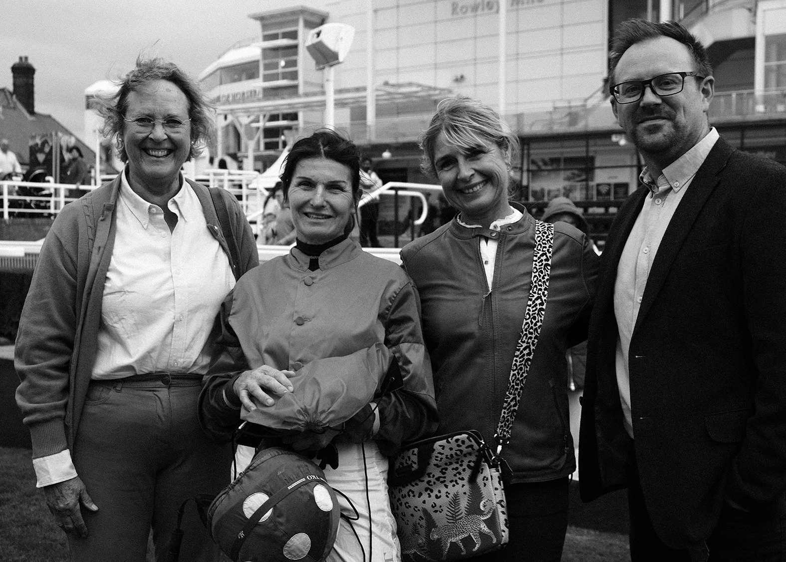 Four people smiling at the camera in an outdoor setting, with a boat and a building in the background.