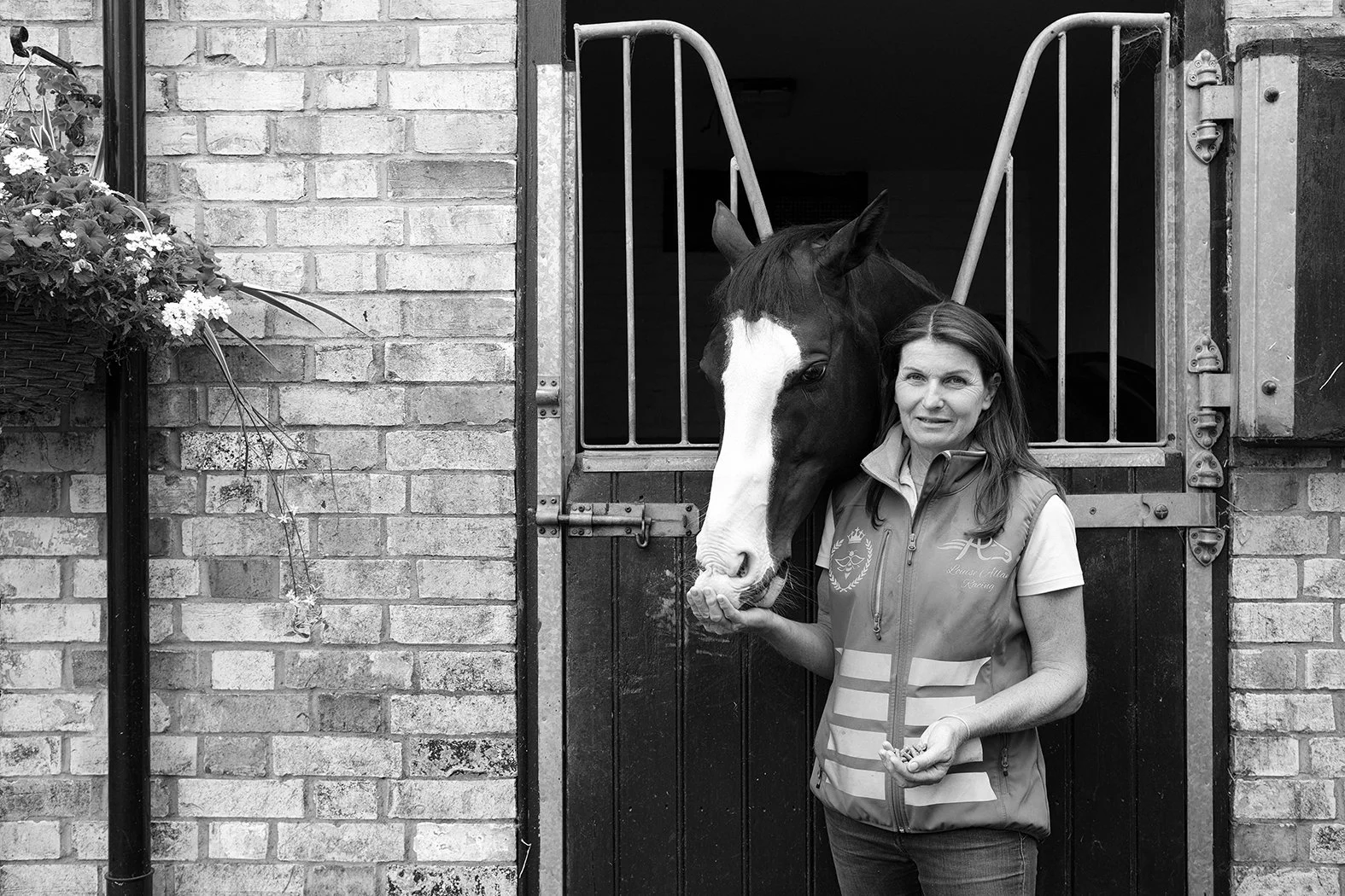 A woman standing in front of a stable door with a horse, holding its nose.
