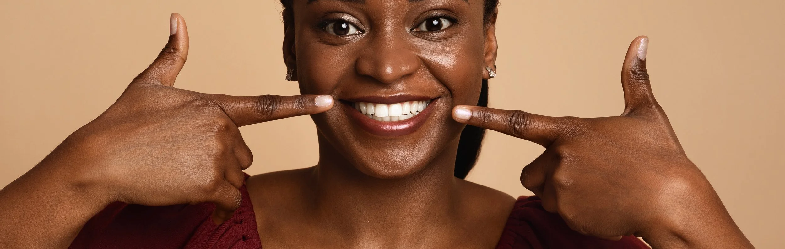 A woman smiling and pointing to her cheeks, showing successful results after a dental filling.