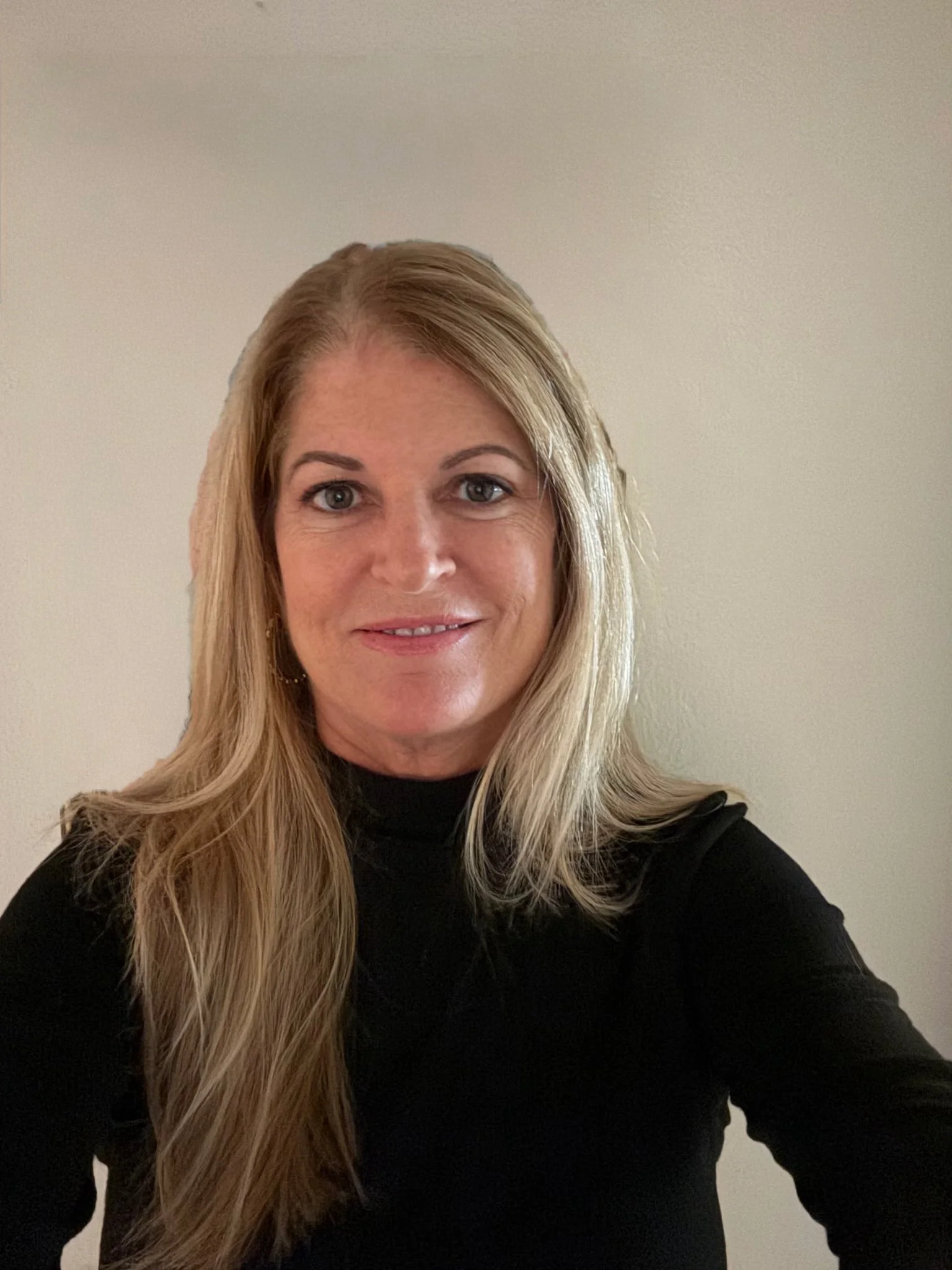 Dental hygienist, Judi, standing against a plain light-colored wall, smiling at the camera.