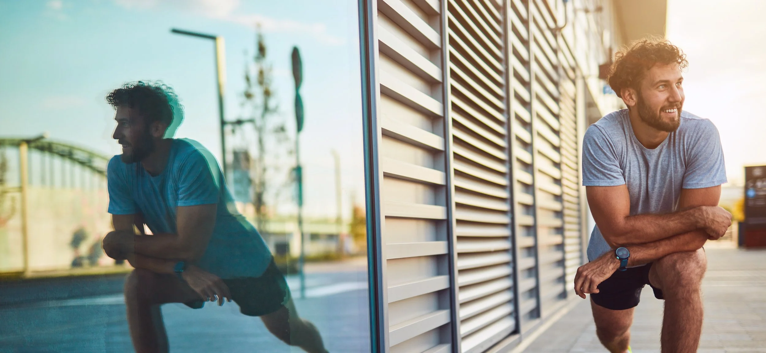 A young man with curly hair and a beard, wearing a gray t-shirt, black shorts, and a smartwatch, stretching his leg outside a modern building with metal siding, during sunset, showcasing the benefits of mouth guards.