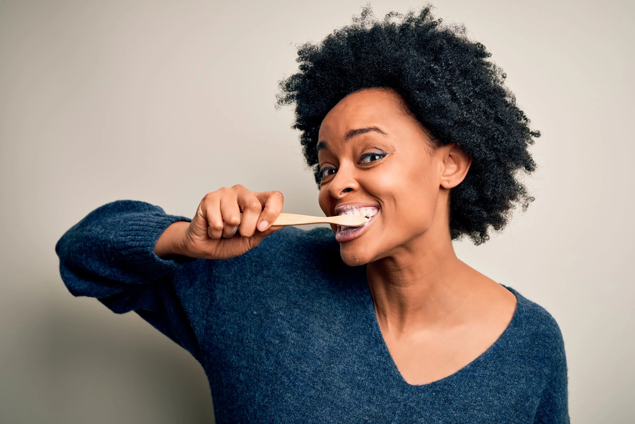a woman wearing a dark blue sweater and brushing her teeth while smiling