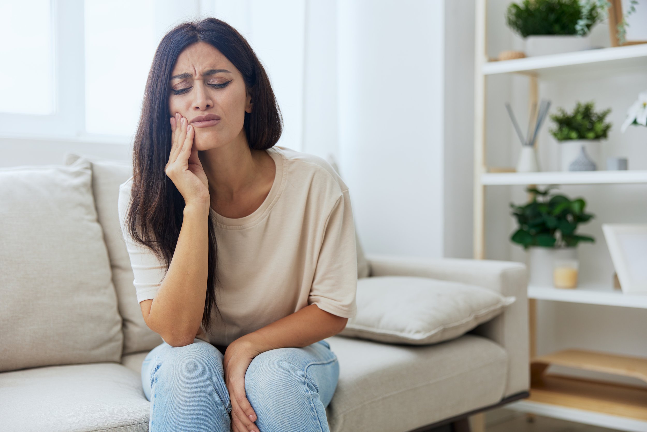 woman with long dark hair holding her cheek with a broken tooth