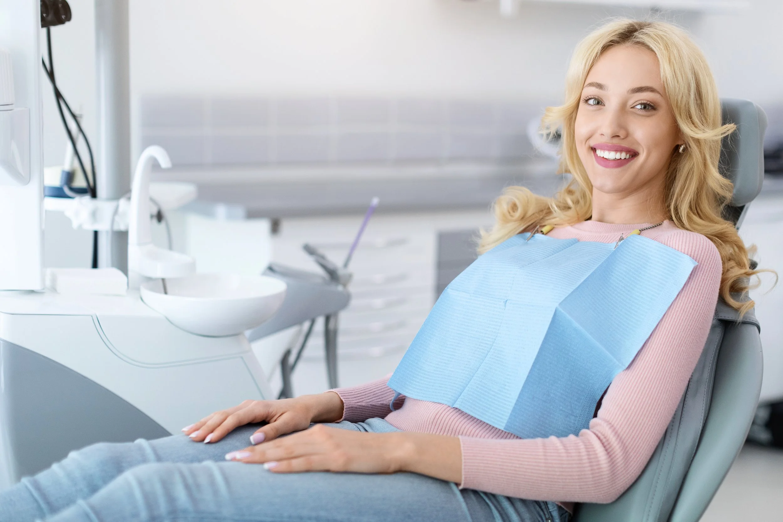 A blonde woman in the patient's seat smiling after receiving excellent dental care