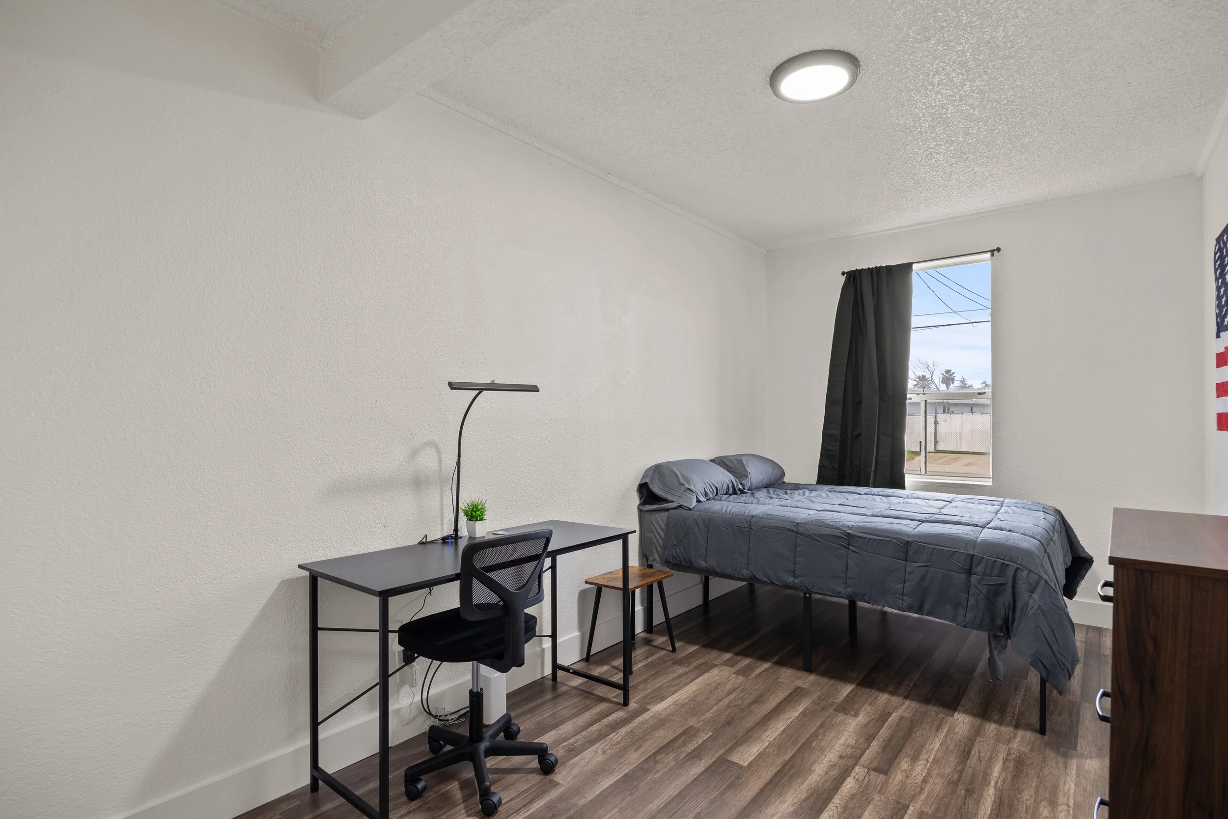 Simple bedroom with a bed, desk, and window with black curtain.