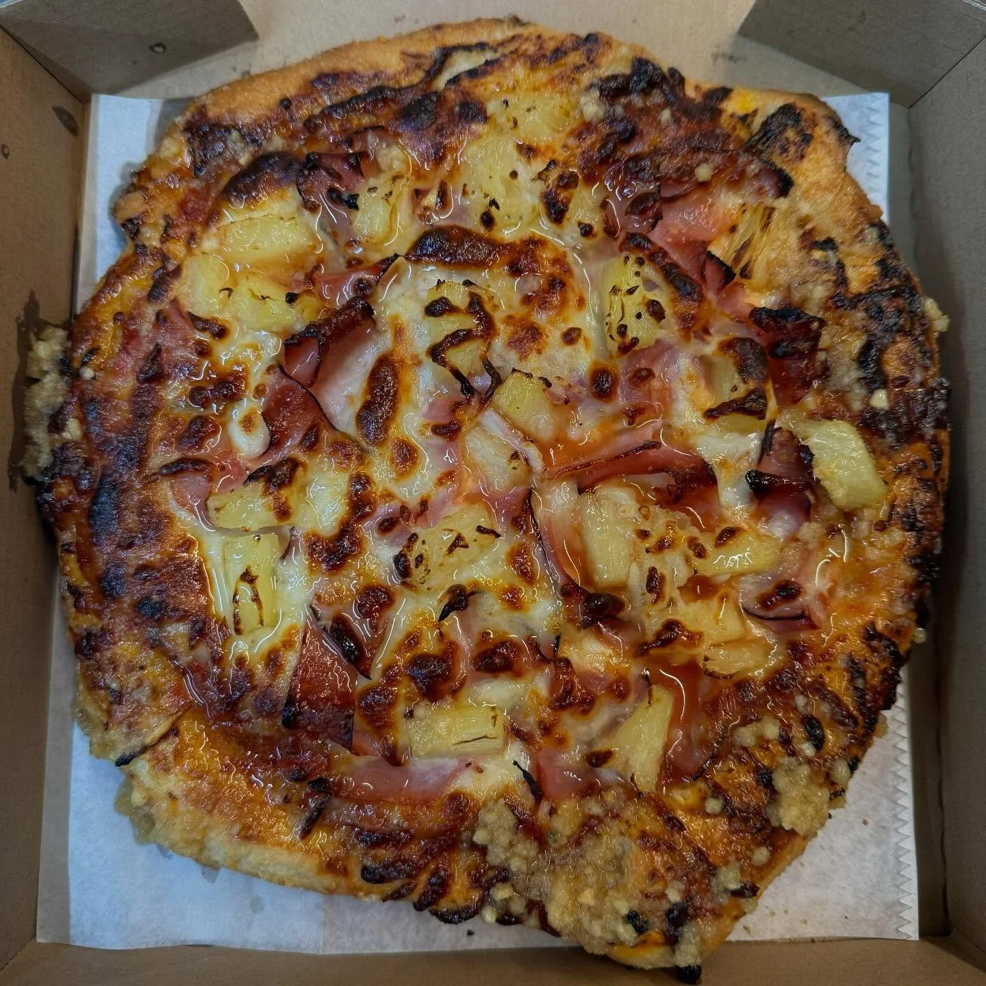 A pizza with pineapple chunks, ham, and bacon in a cardboard box.