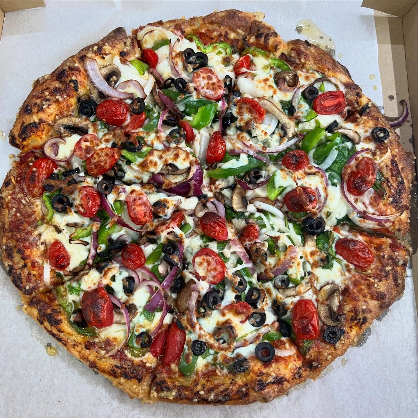 A freshly baked pizza topped with cherry tomatoes, black olives, green peppers, red onions, mushrooms, and melted cheese.