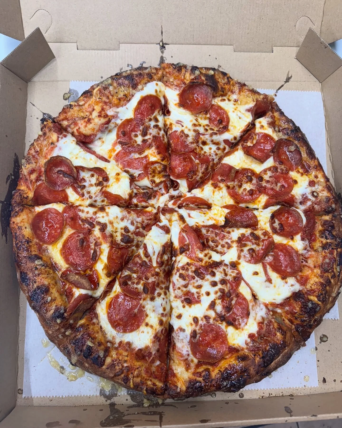 A pepperoni pizza in a cardboard box with melted cheese and a slightly charred crust.