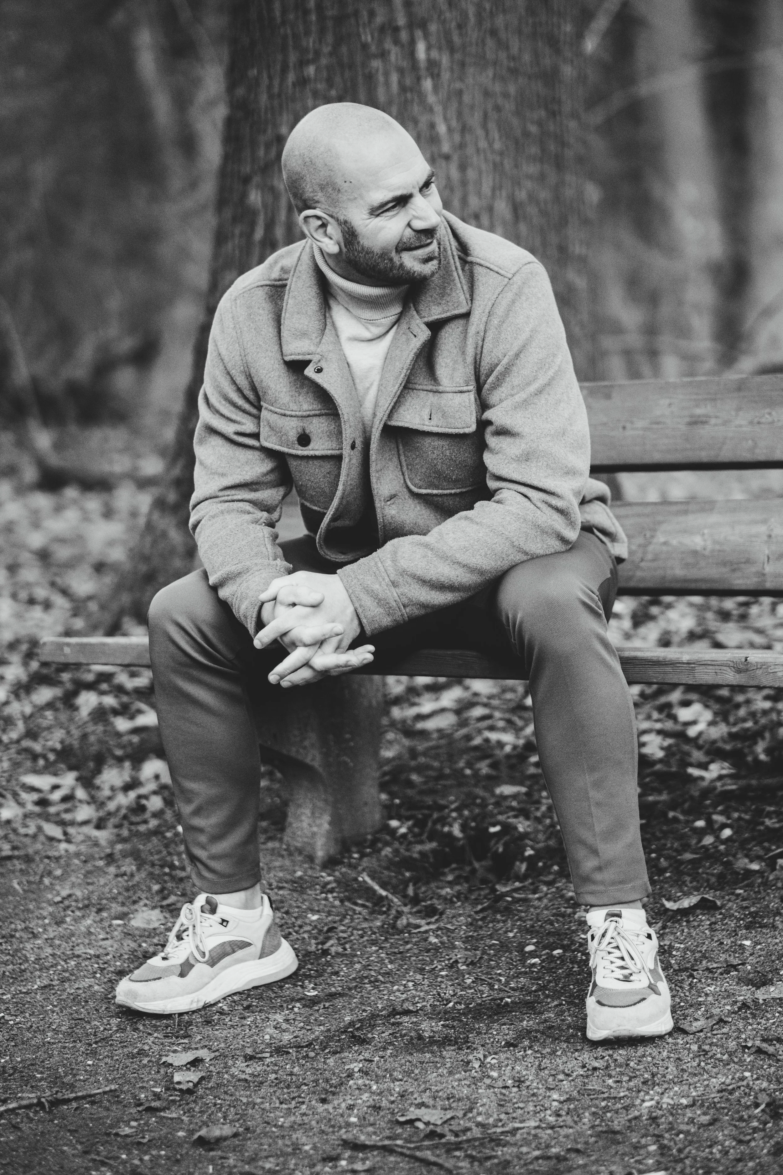 Zwarte en witte foto van een man zittend op een bankje in een park, omgeven door bomen.