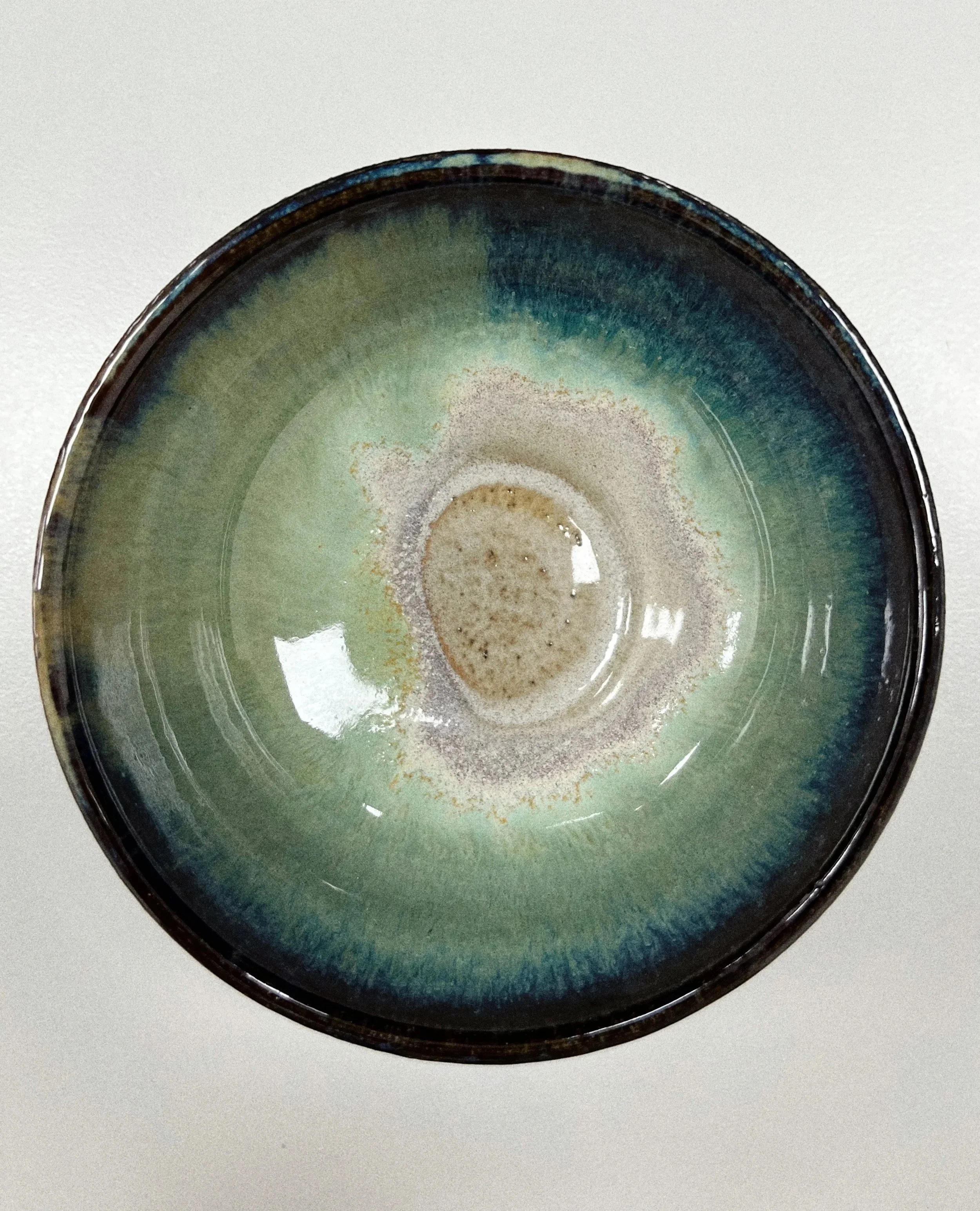 A ceramic bowl with a green and blue glazed interior, containing some foam or froth, viewed from above.