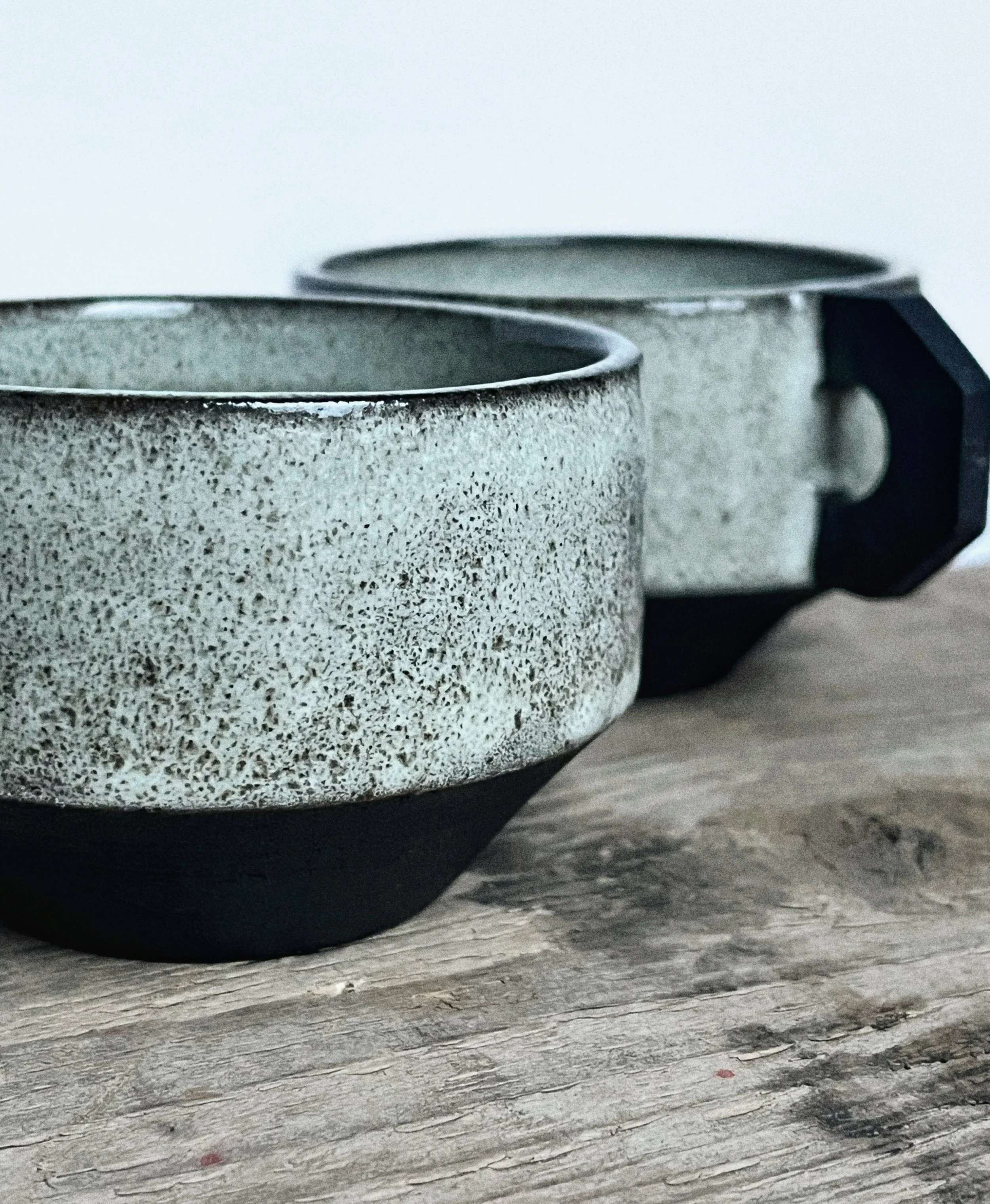 Two speckled ceramic cups with black bases and handles on a rustic wooden surface.