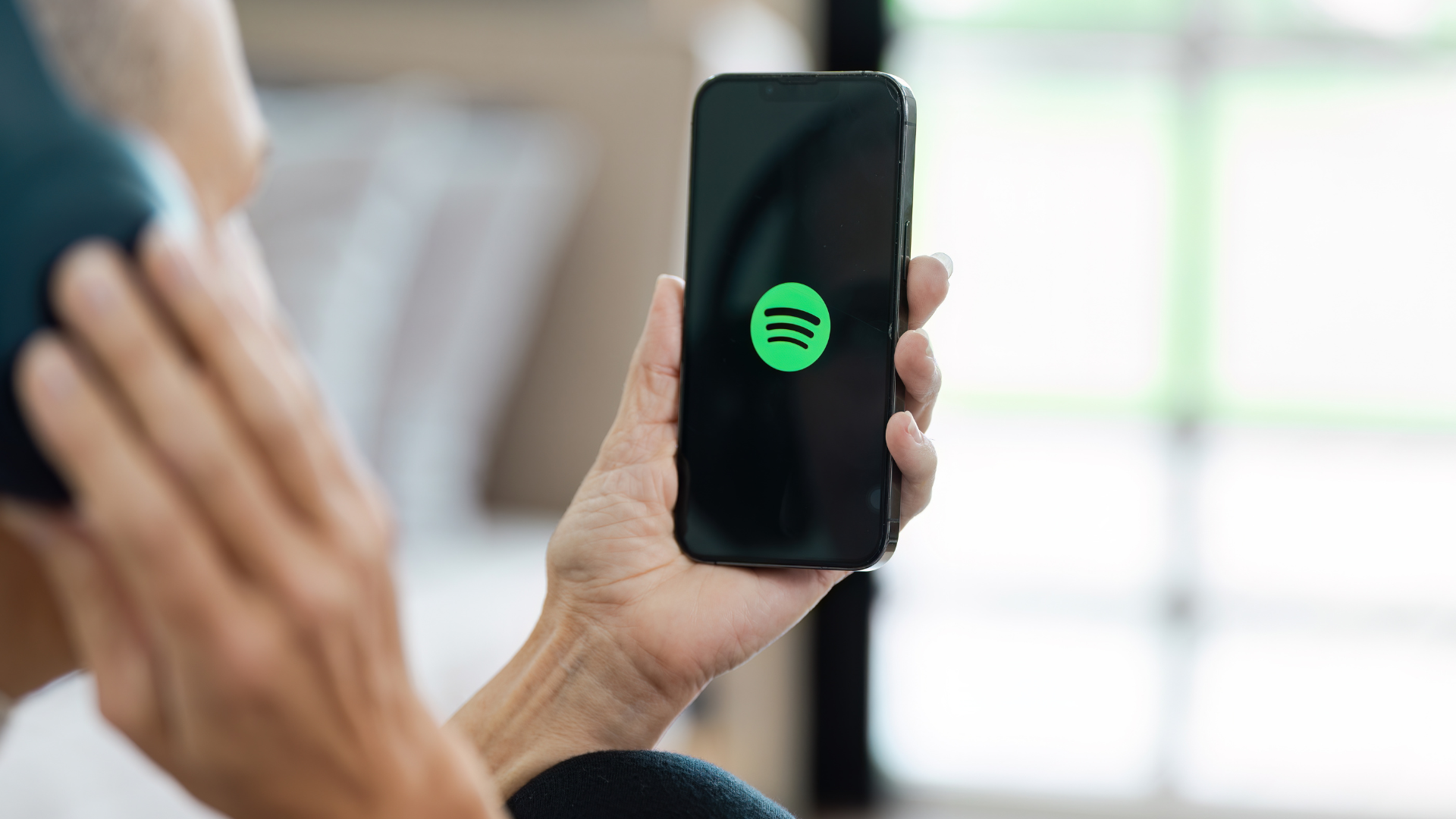 Persoon houdt een smartphone met het Spotify logo op het scherm, luisterend met een koptelefoon.