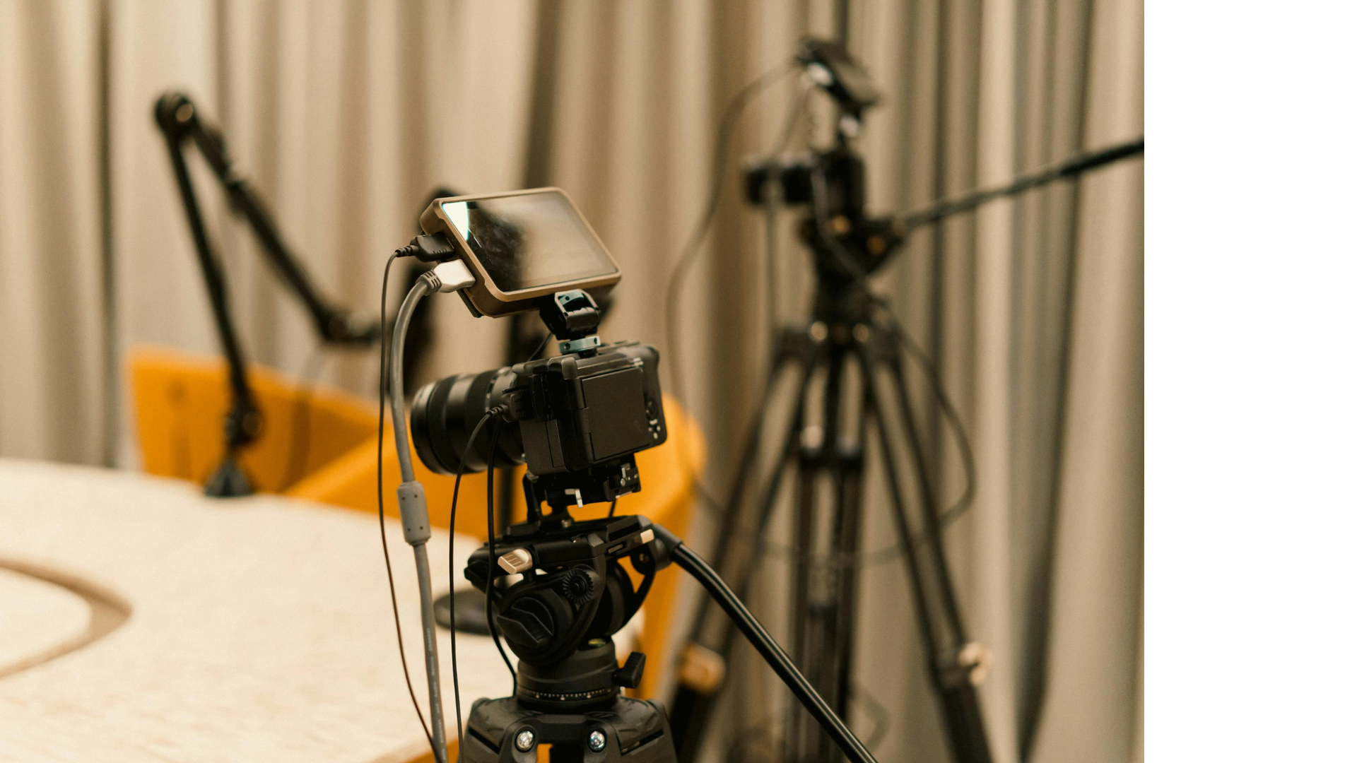 Podcast studio met camera op statief, met andere cameraopstelling op de achtergrond.
