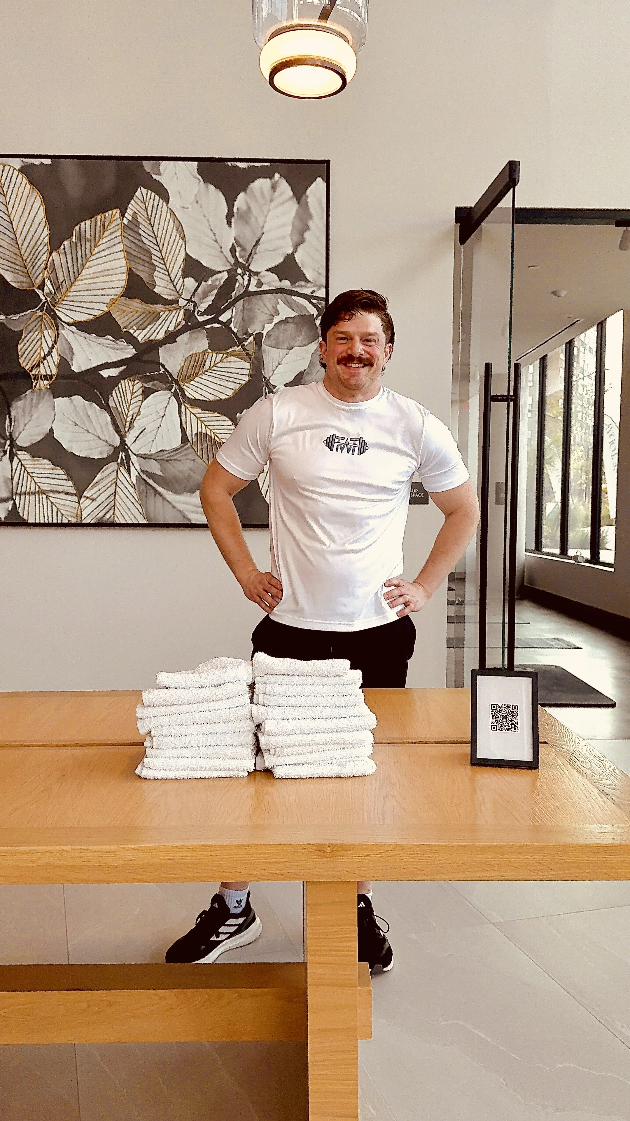 A personal trainer standing behind a welcome table in a reception area, smiling.
