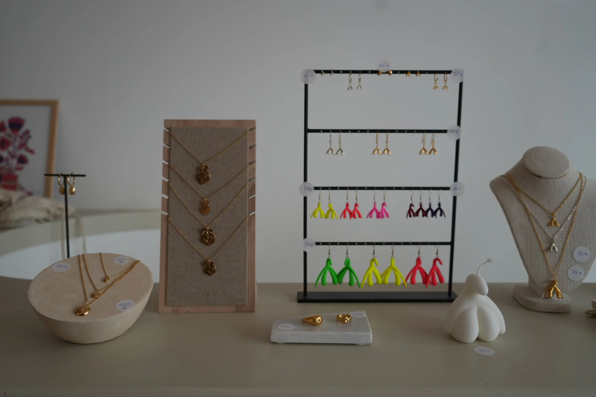 Vitrine avec bijoux en or, colliers, boucles d'oreilles colorées, et pendentifs, présentés sur des supports en bois et en tissu, avec une structure de présentation métallique.