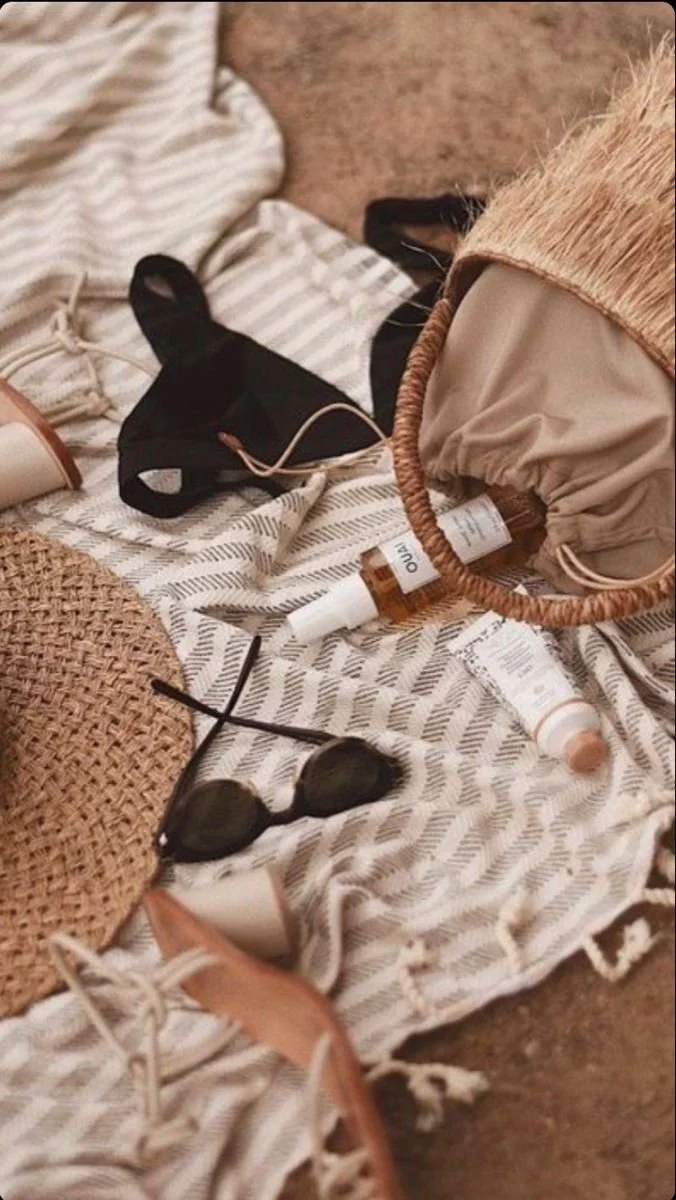 Beach or poolside scene with a striped fabric, black face mask, a pair of sunglasses, and various cosmetic bottles, suggesting a relaxing summer day.