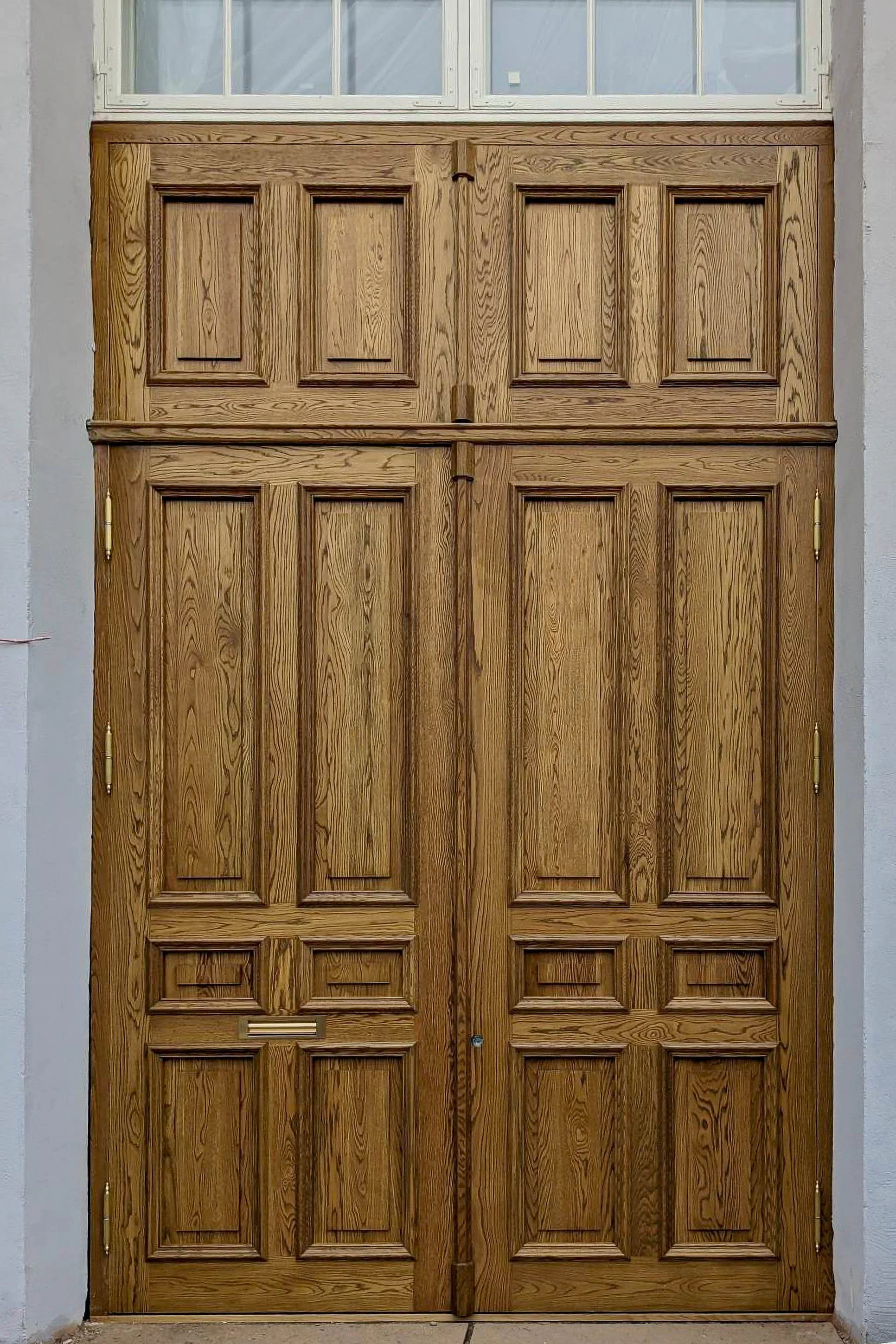 Wooden double doors with a mail slot and window at the top.