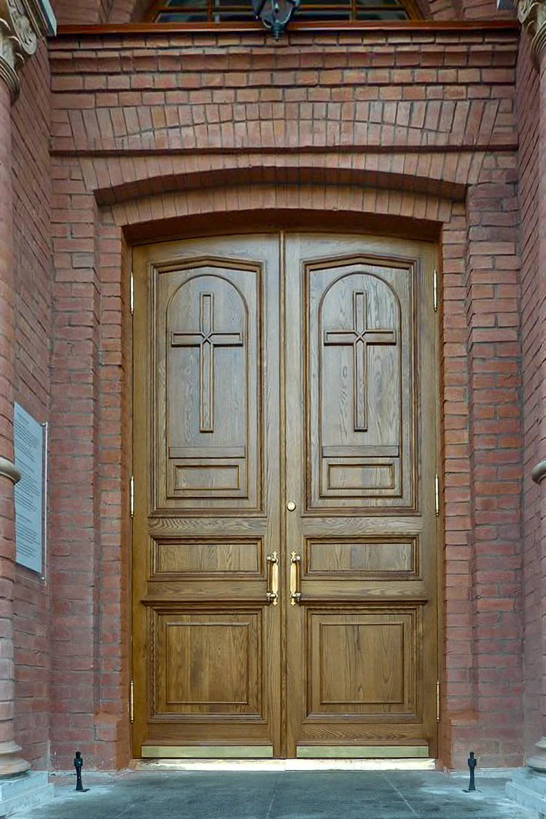 Wooden double doors with crosses carved on them, set within a brick archway.