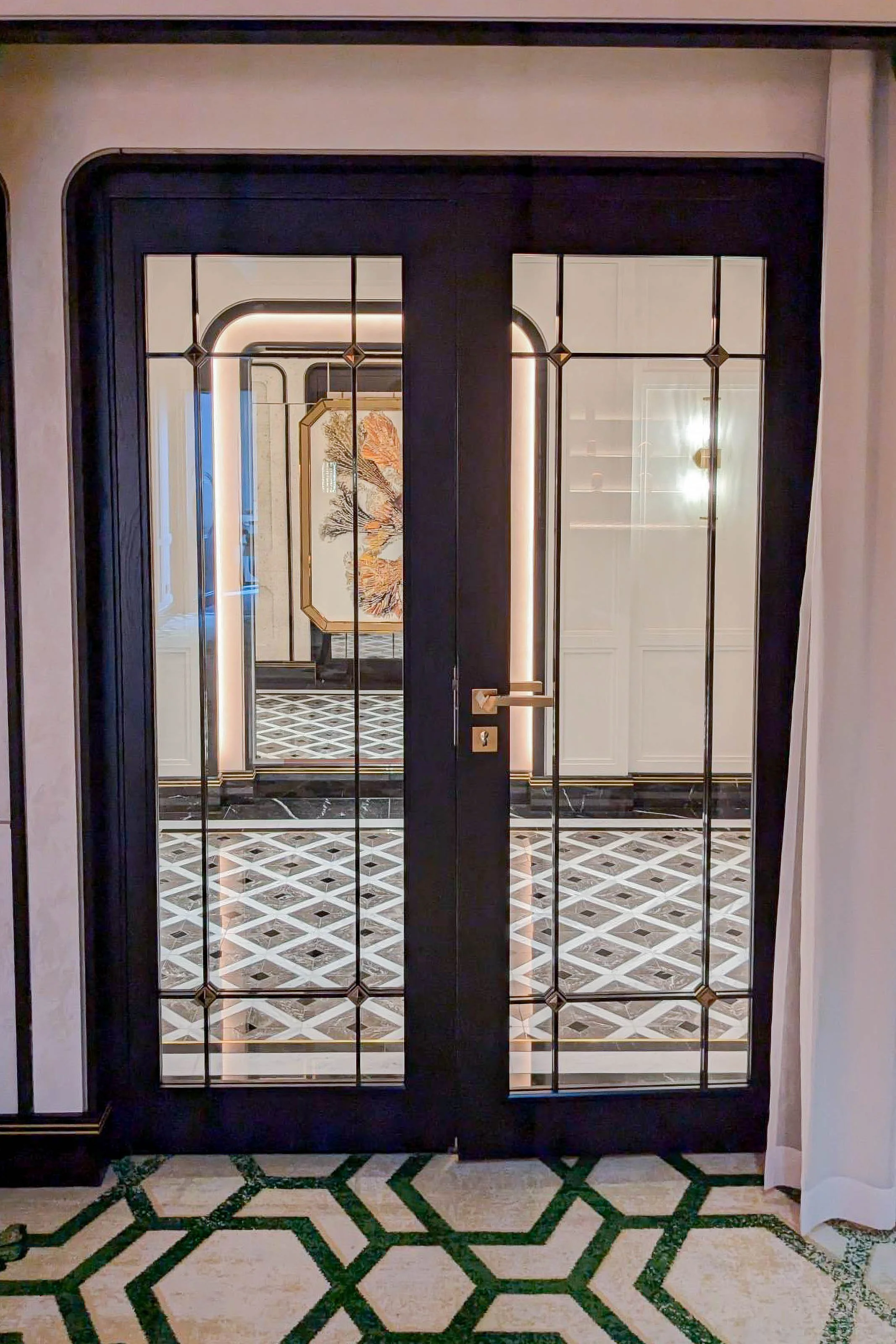 View through glass double doors into a stylish interior with geometric flooring, a framed artwork on the wall, and built-in white cabinetry.