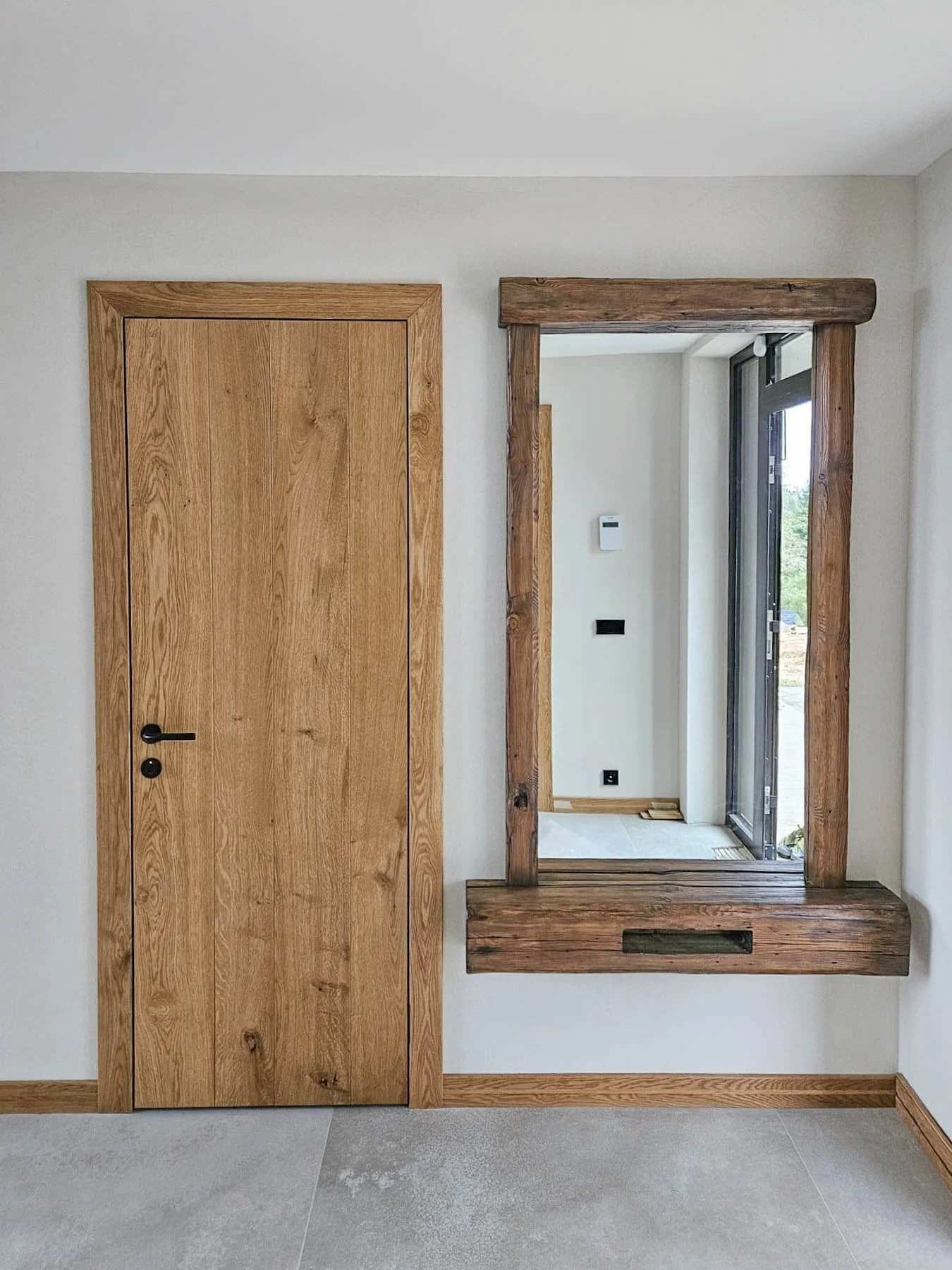 A wooden door and a mirror with a wooden frame, both mounted on a white wall.