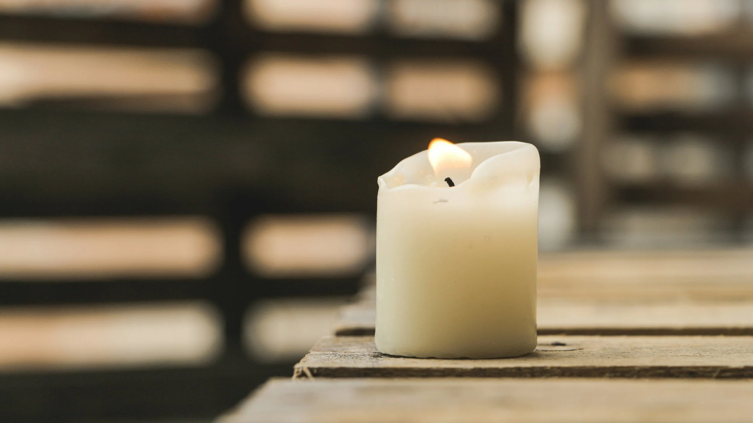 A lit white candle placed on a wooden surface with a blurred background.